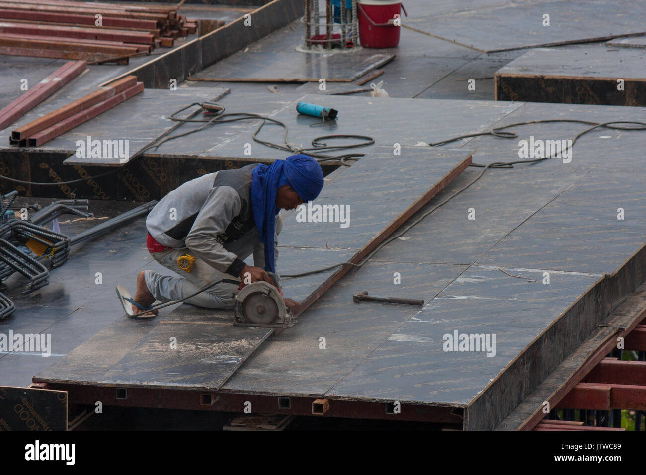 Ein thailändischer Bauarbeiter in Flip Flops verwendet eine Kreissäge ein Stück Holz auf einer Baustelle in Bangkok, Thailand zu schneiden Stockfoto