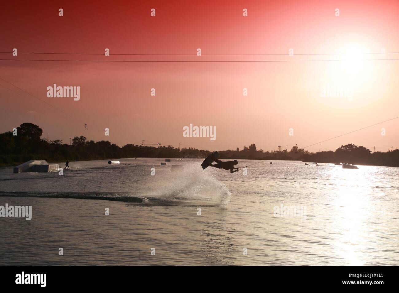 Wake Boarder in Mid-Air tun Half-Somersault auf dem See bei Sonnenuntergang hinter Plume von Spritzwasser durch Rot abgestufte Filter Sky akzentuieren Stockfoto