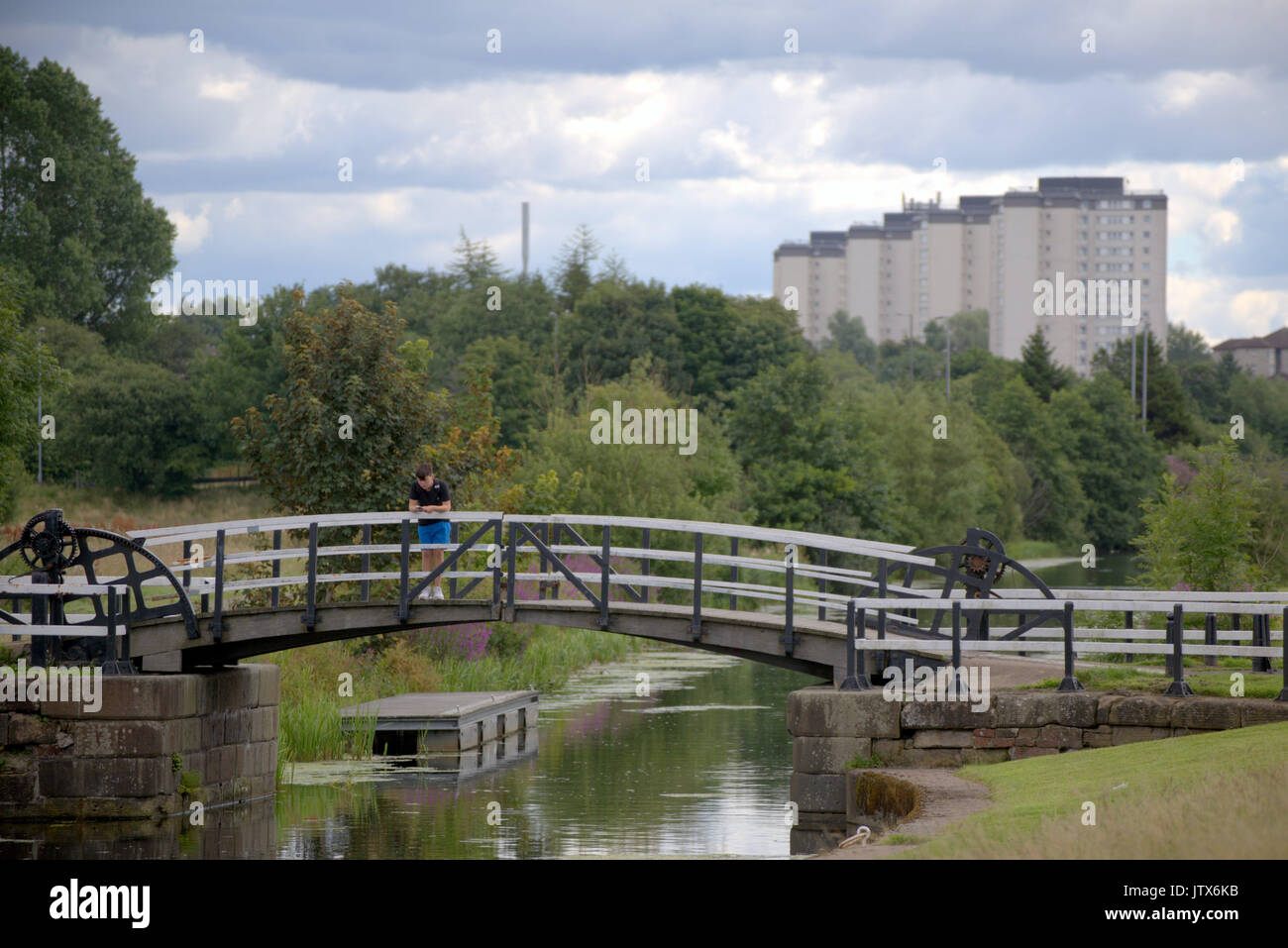 Clydebank, Glasgow Blairdardie highflats im Hintergrund. Junge verwendet Smartphone als Sommer Wetter liefert auf der Forth-and-Clyde-Kanal Brücke Stockfoto