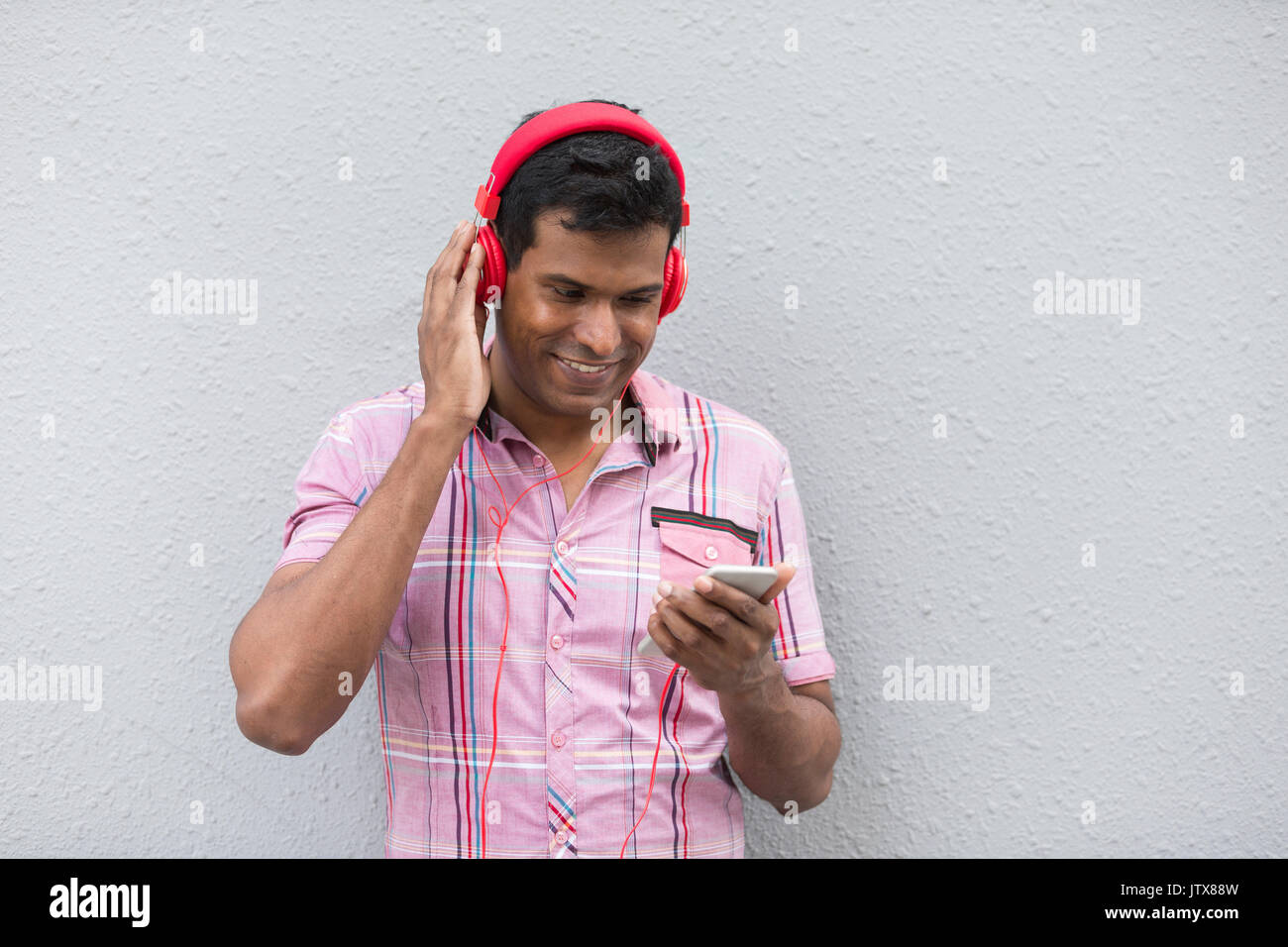 Inder mit einem Smartphone. Asiatischer Mann mit Smart Phone, gegen eine graue Wand gelehnt. Stockfoto
