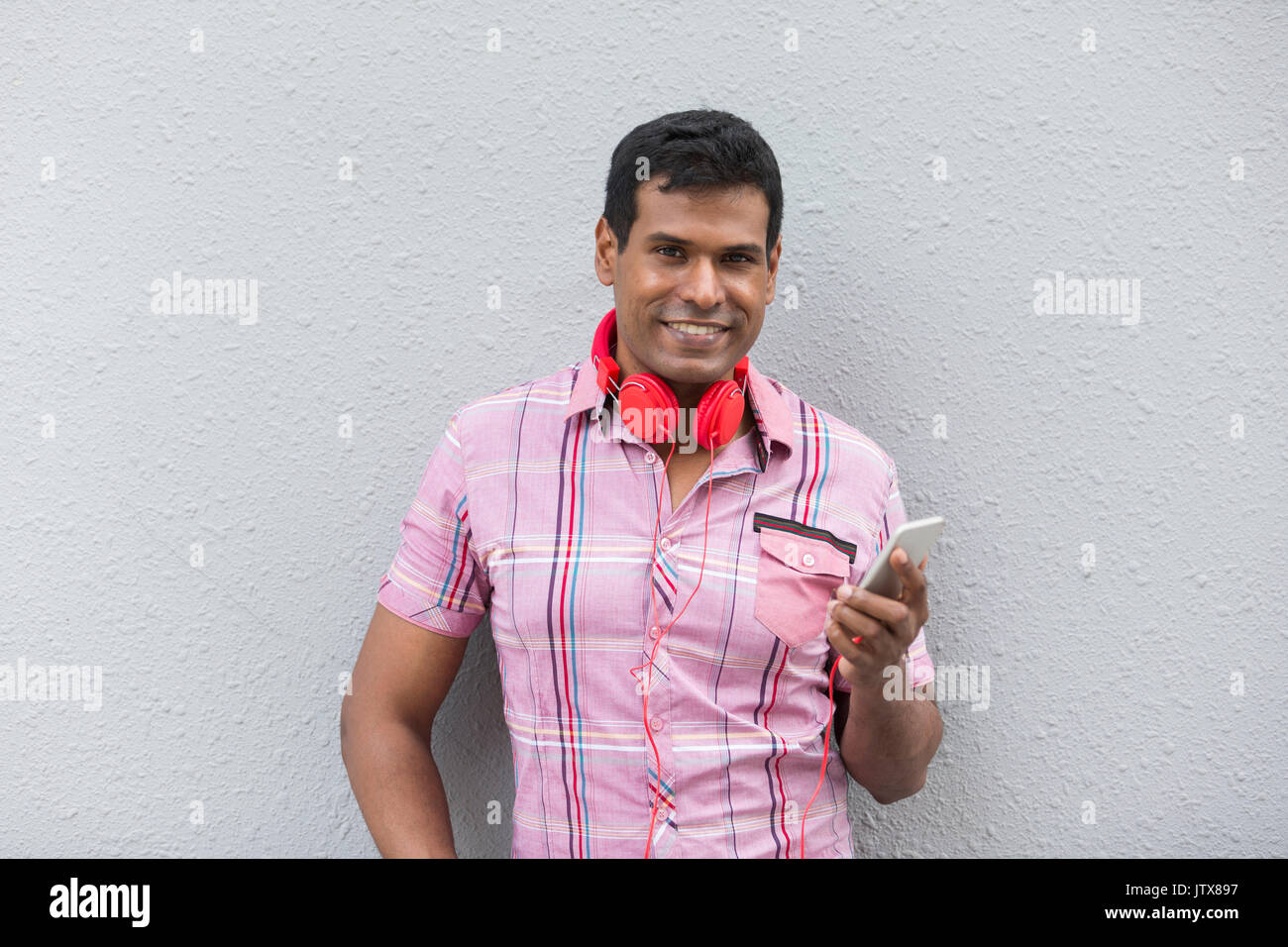 Inder mit einem Smartphone. Asiatischer Mann mit Smart Phone, gegen eine graue Wand gelehnt. Stockfoto