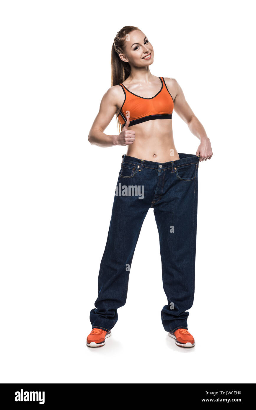 Sportlerin das Tragen von Jeans in Übergröße ihren schlanken Körper zu zeigen, während der Daumen zeigt, isoliert auf weißem Stockfoto