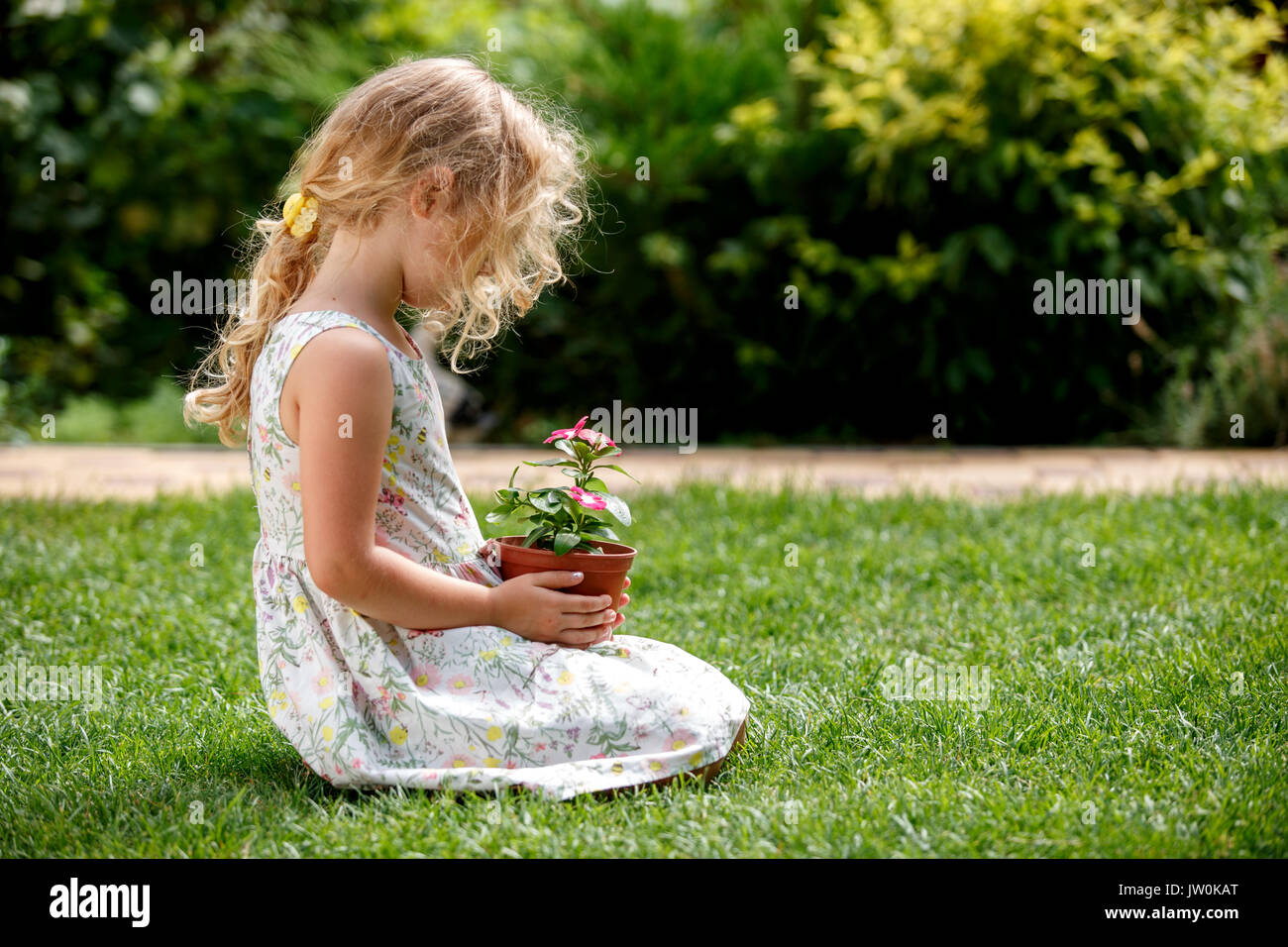 Kleine blonde Mädchen, dass junge Blume Pflanze in den Händen auf grünem Hintergrund. Stockfoto