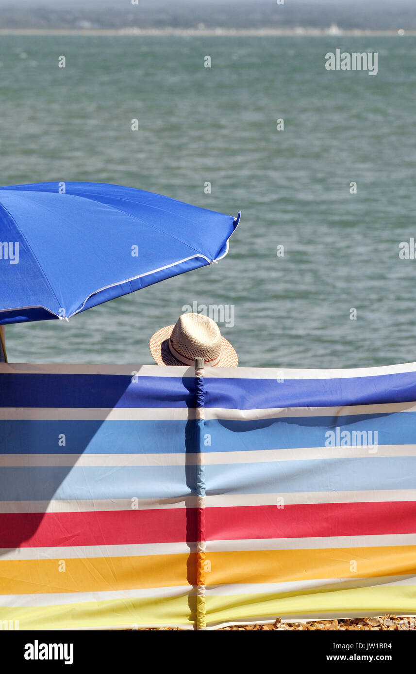 Ein Mann mit einem Sommer schatten Panama Hut sitzen unter einem  Regenschirm oder Sonnenschutz hinter einem Windschutz mit nur seinen Kopf  angezeigt. Farbenfrohe Wind brechen Stockfotografie - Alamy