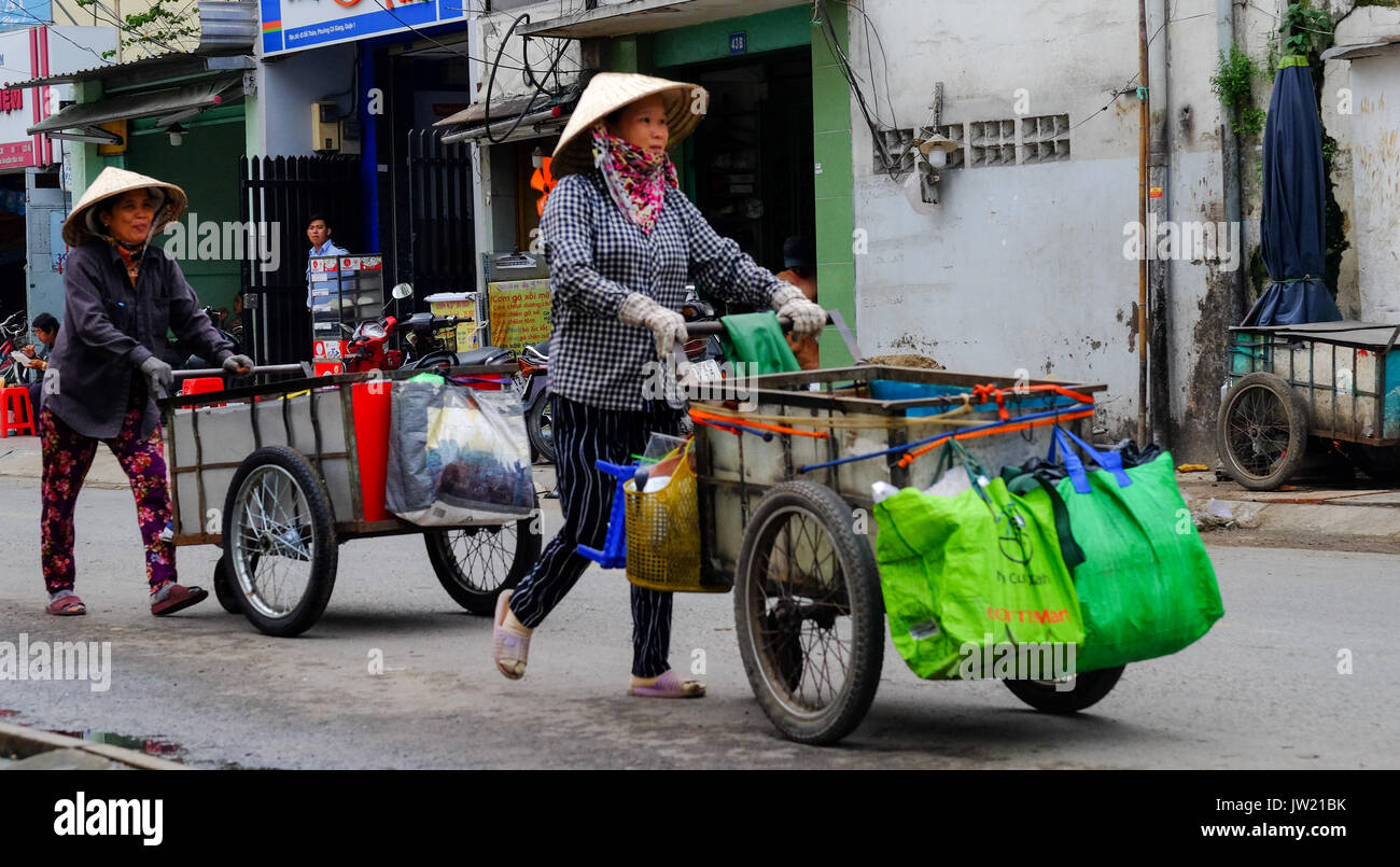 Zwei weibliche Vietnamesische Straßenhändler drücken sie ihre Karren entlang einer Straße in Ho Chi Minh City, Vietnam Stockfoto