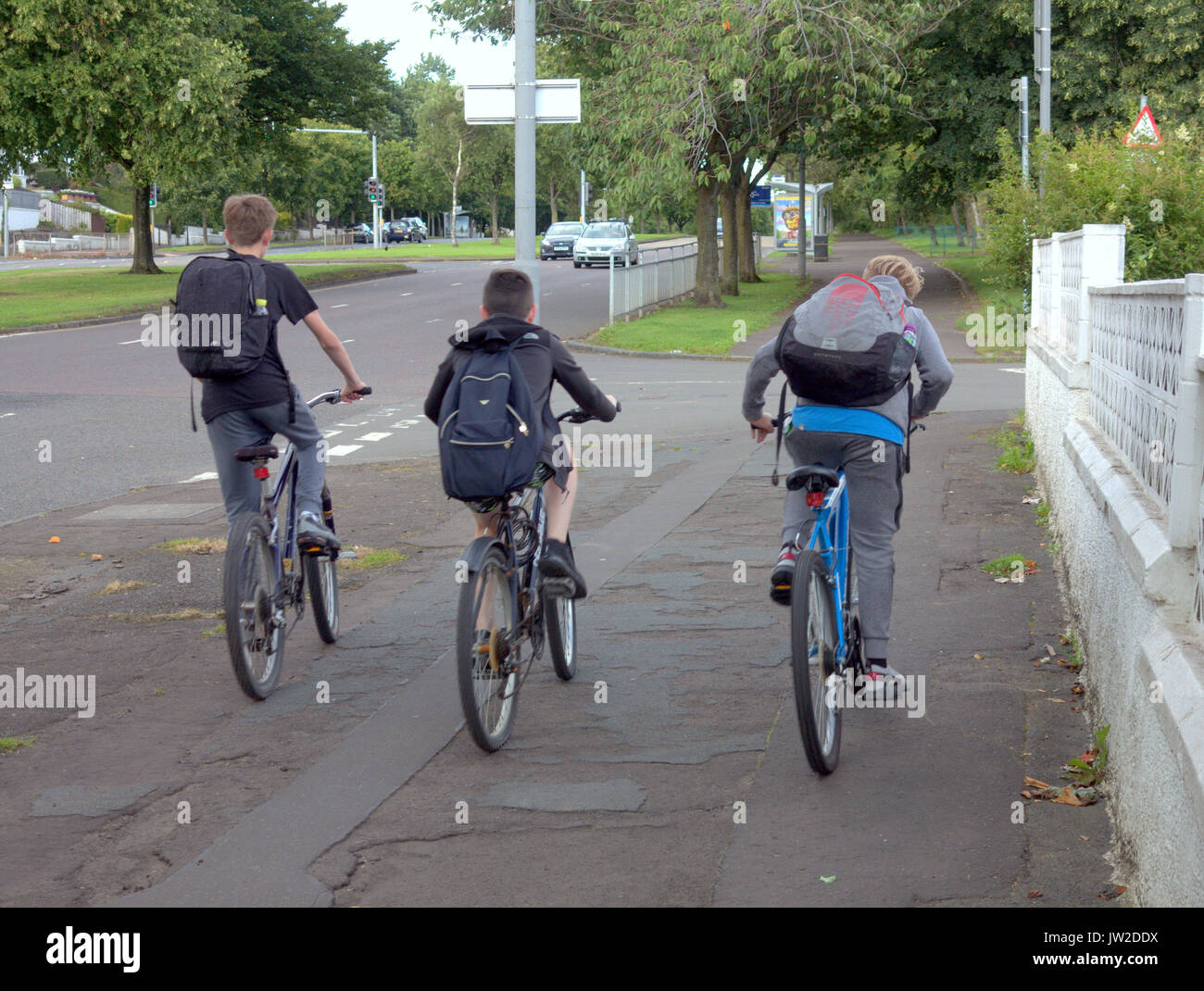 Drei Jungen auf dem Fahrrad fahren auf dem Bürgersteig genießen Sommer Urlaub oder Reisen mit Taschen zur Schule Stockfoto