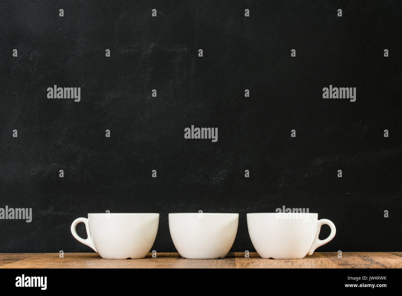 Drei weiße Kaffeetassen arrangiert zusammen auf retro Holz Textur Stock mit schwarzen Schiefertafel Wand Hintergrund im Restaurant Studio platziert. Stockfoto