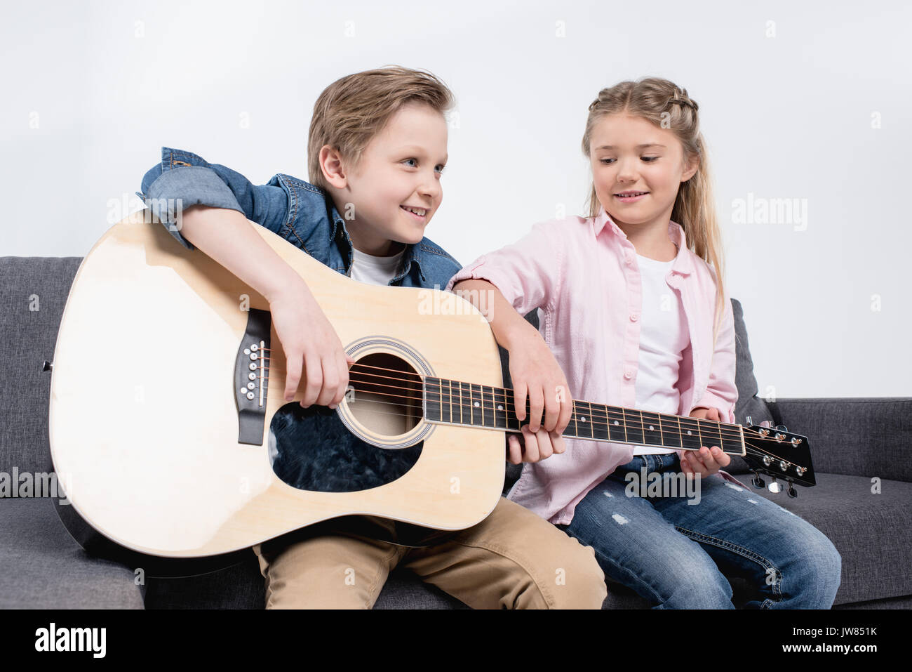 Gerne Bruder und Schwester spielen auf der Gitarre zusammen beim Sitzen auf dem Sofa Stockfoto