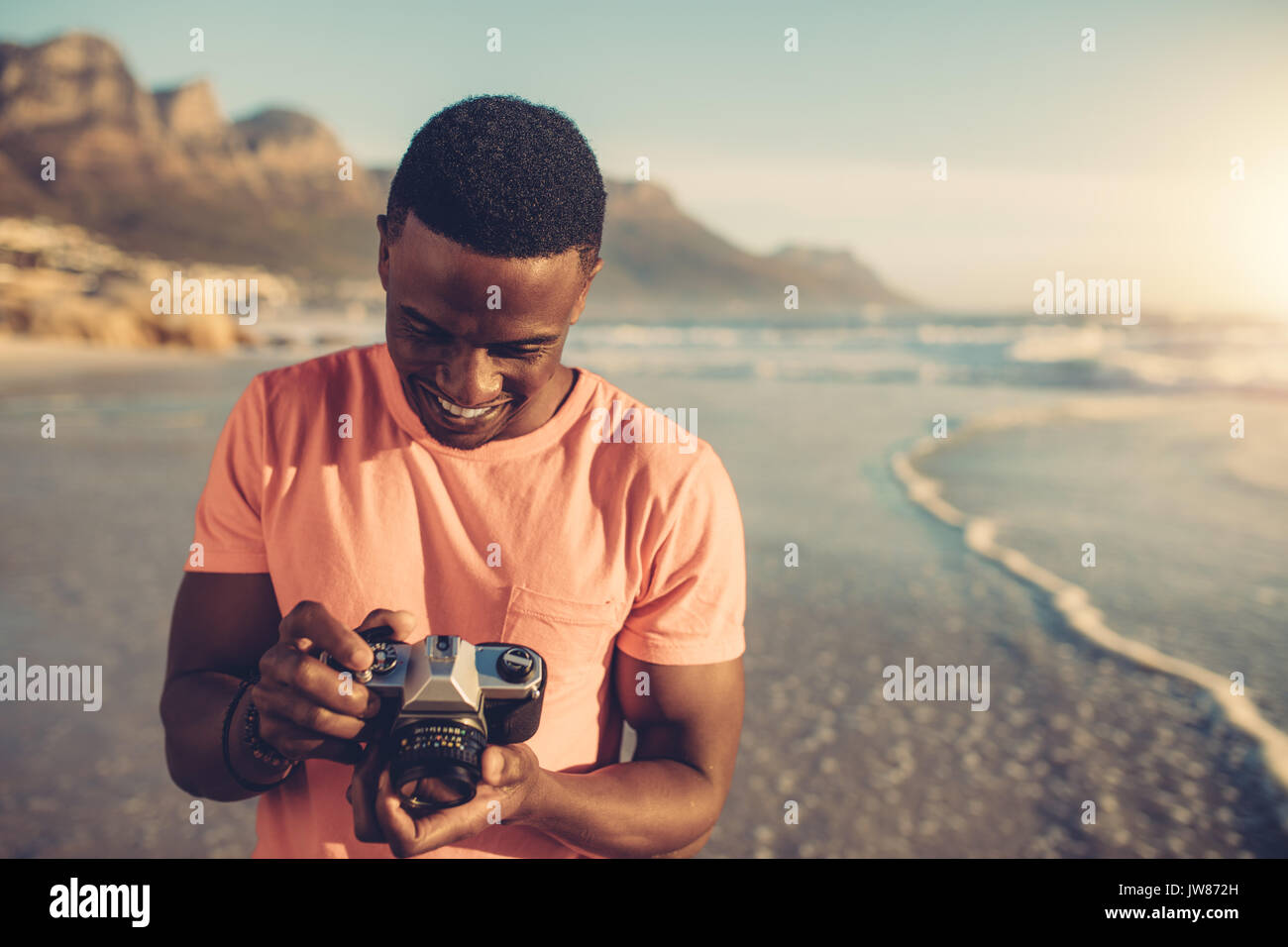 Afrikanischer mann Kontrolle Fotos in seine digitale Kamera. Junger Mann mit der Digitalkamera auf den Strand. Stockfoto