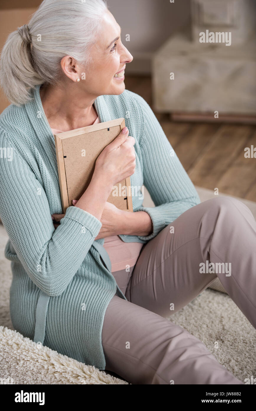 Lächelnd senior Frau umarmen Bilderrahmen und Wegsehen Stockfoto