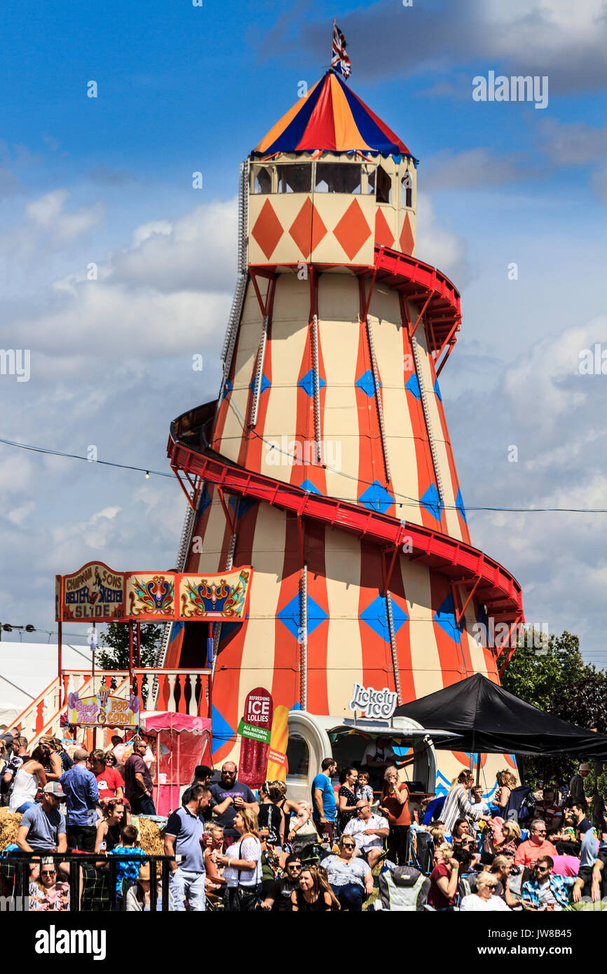 Menschenmengen sammeln in der Nähe der Stände- und Unterhaltungsviertel, mit einem traditionellen Helter Skelter Spiralrutsche, Jimmy's Festival, Ipswich, Suffolk, Großbritannien Stockfoto