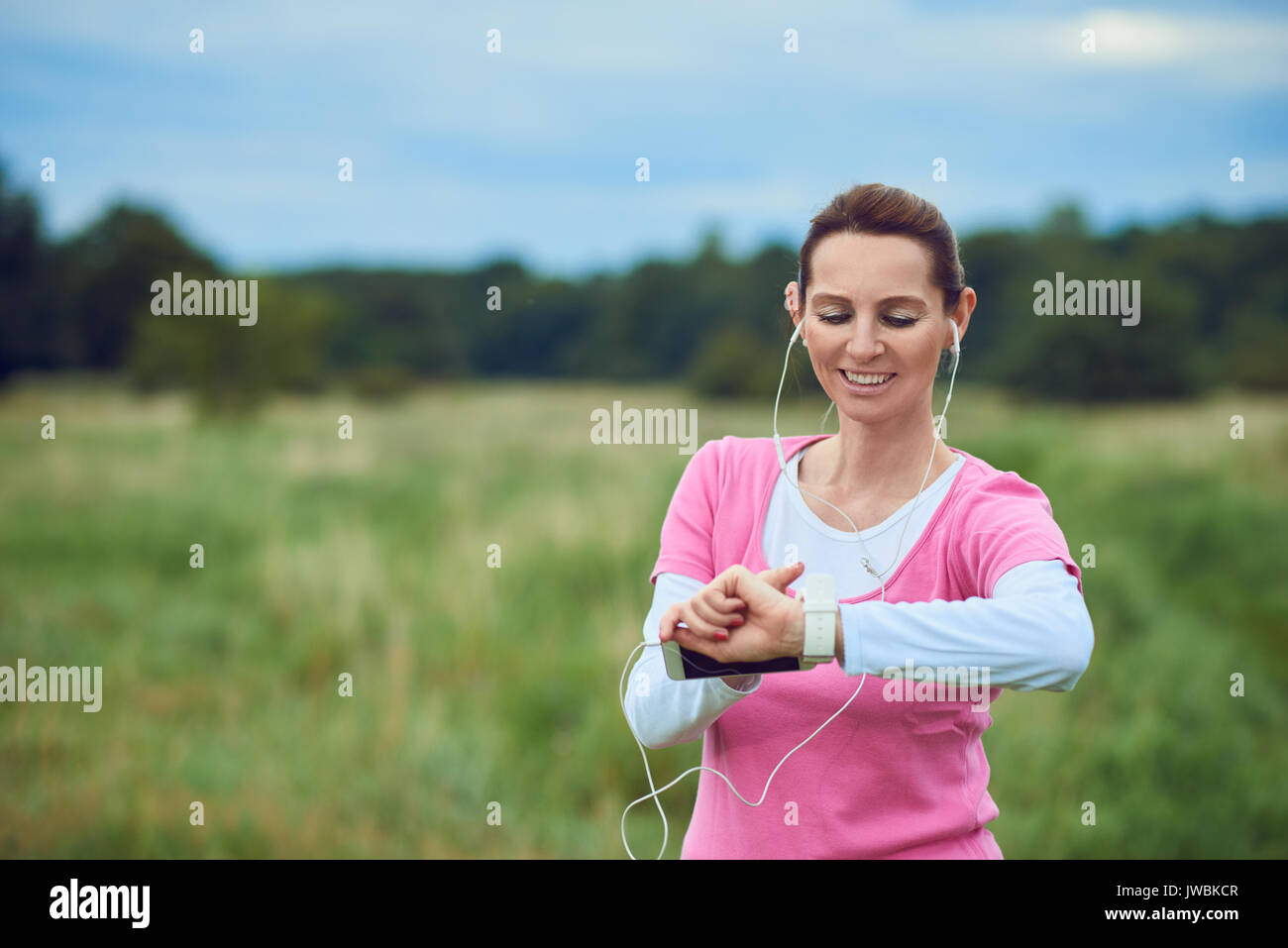 Frau mittleren Alters ihr Sport oder Gesundheit Uhr Kontrolle beim Joggen in der Natur hören von Musik auf Ihr Handy in einer gesunden lifestyl Stockfoto
