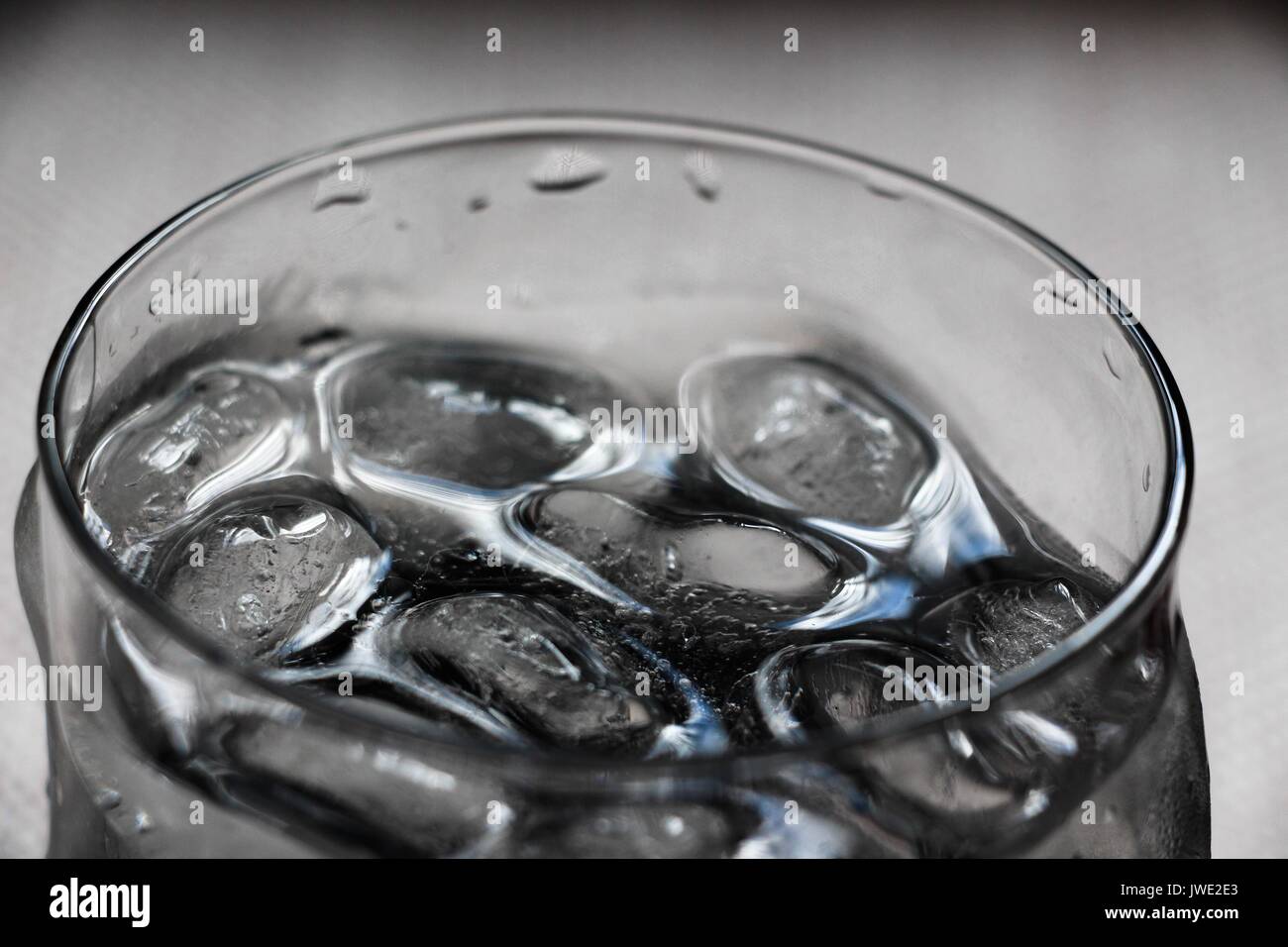 Stücke von kaltem Eis Schwimmer im Wasser, das in ein durchsichtiges Glas gegossen wird. Das Wasser gekühlt, und es werden alle Durst mit seiner Frische stillen. Stockfoto