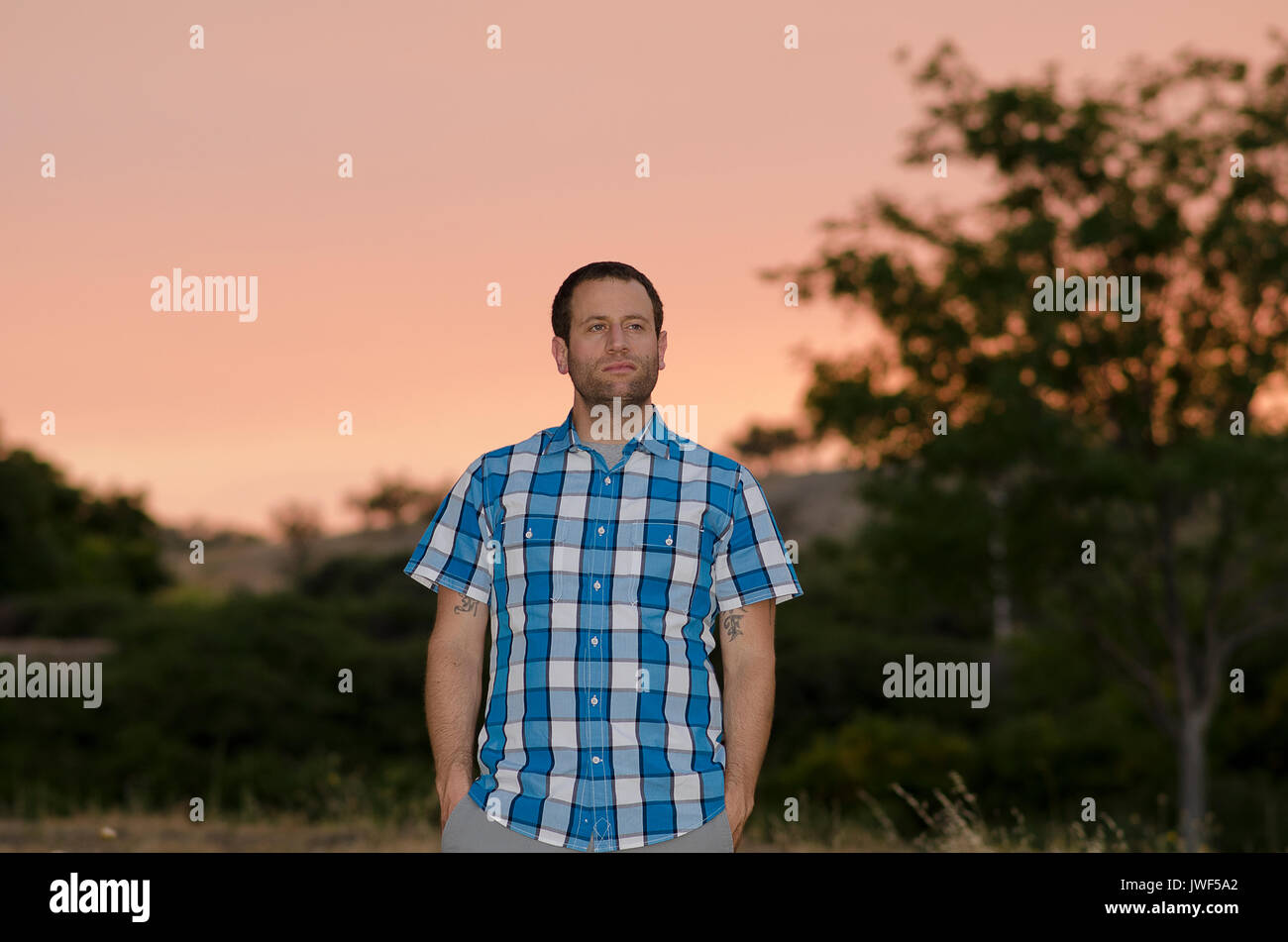Mann mit Händen in den Taschen bei Sonnenuntergang, Blick nach rechts. Stockfoto