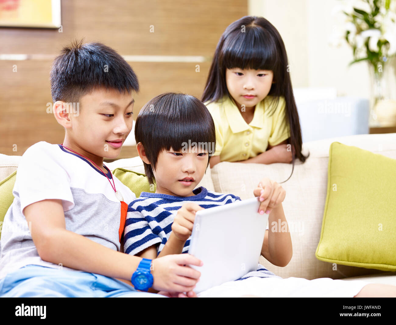 Drei asiatische Kinder sitzen auf der Couch zu Hause spielen video game mit digitalen Tablet. Stockfoto