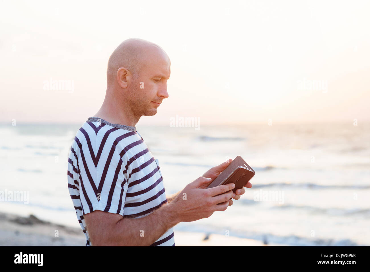 Mann mit Handy, der am Ufer des Meeres Stockfoto