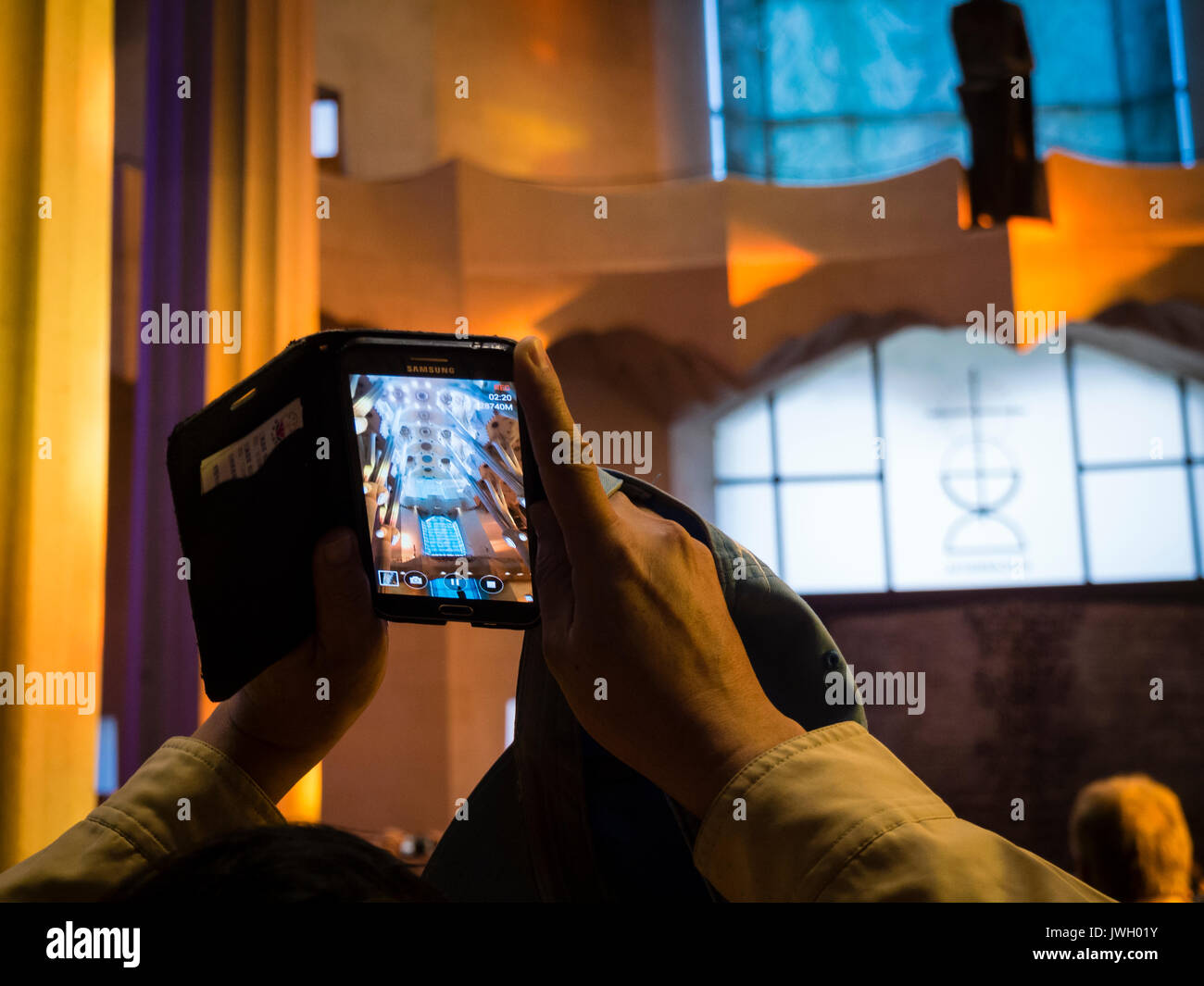 Ein Tourist ist das Aufnehmen von Fotos mit einem Smartphone innerhalb des Barcelona Sagrada Familia Kathedrale, mit Besuchern aus aller Welt überfüllt ist. Die Stockfoto