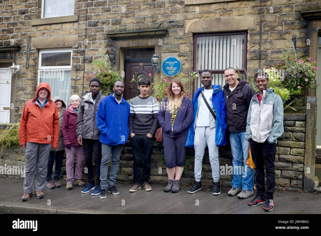 Hayfield, Derbyshire, UK. 12 Aug, 2017. Vier Flüchtlinge aus dem Sudan und aus Pakistan ein Tag in Derbyshire genießen. Die Flüchtlinge, die jetzt leben in Derby, nach Monaten in den Dschungel von Calais, Frankreich. Nach einer kurzen Besichtigung von Hayfield Dorf Sie auf einer fünf Kilometer zu Fuß über die Derbyshire Hügeln bei Kinder ging. Hier, Sie stellen mit Helfer ausserhalb des blauen Plakette anzeigt, wo Arthur Lowe, Star der TV-Programm Dad's Army, geboren wurde. Quelle: John Fryer/Alamy leben Nachrichten Stockfoto