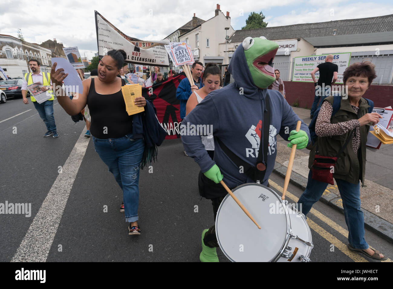 London, Großbritannien. 12. August 2017. Ein Schlagzeuger in einen Frosch Outfit auf der Focus E 15 Mütter März von Ferrier Punkt in Canning Town zu einer Kundgebung an Tanner Punkt in Plaistow weisen auf die Gefahr der beiden Bausteine mit den gleichen Mantel als Grenfell Tower, anspruchsvolle sichere Wohnungen, nicht soziale Säuberungen in East London. Sie setzte dann den Zimmerleuten Immobilien in Stratford weitgehend von Menschen über 10 Jahren geleert und will zu demolieren, für einen 'Hände um Solidarität bei den Zimmerleuten Immobilien" gegen Dekantieren, demolit Credit: Peter Marschall/Alamy leben Nachrichten Stockfoto
