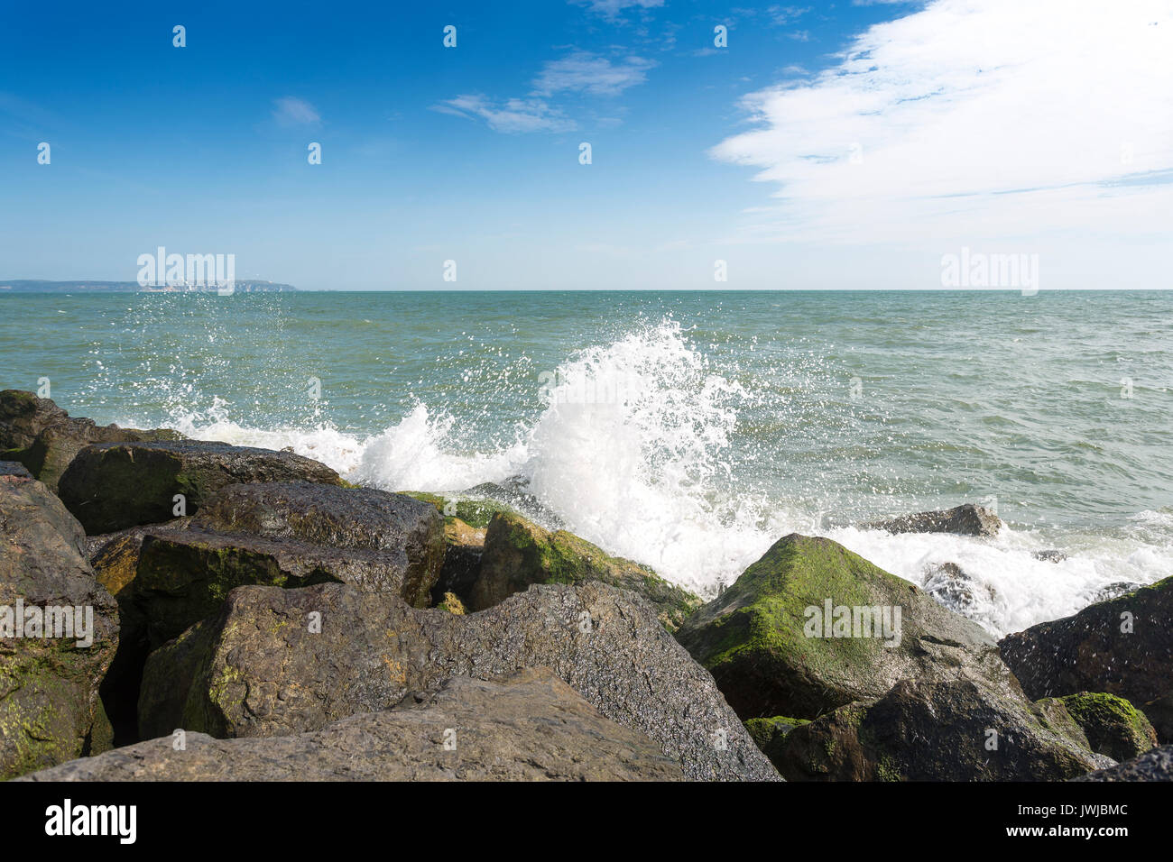 Wellen, die auf steinigen Strand und Felsen, mit blauem Himmel und Wolken. Avon Strand, Christchurch, Hampshire, Großbritannien Stockfoto