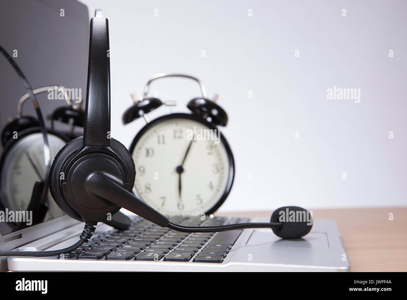 Laptop mit einem Headset auf der Tastatur und Wecker hinter closeup niedrigen Winkel über die Tasten mit Kopie Raum gesehen Öffnen Stockfoto