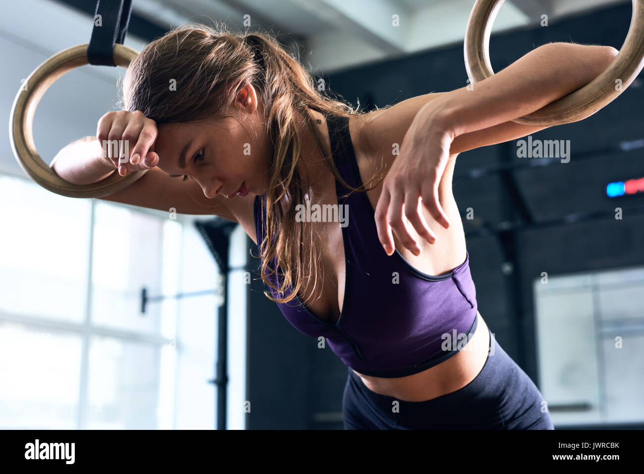 Porträt der jungen schönen Frau vom Training lehnte sich auf Gymnastik Ringe beim crossfit Workout im modernen Fitnessraum erschöpft Stockfoto