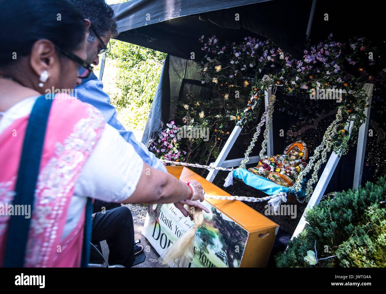 Menschen swing baby Krishna während der janmashtami Hindu Festival in der Hare Krishna Bhaktivedanta Manor in Watford, eine jährliche Hinduistische fest, dass feiert die Geburt von Krishna, der achte Avatar von Vishnu. Stockfoto