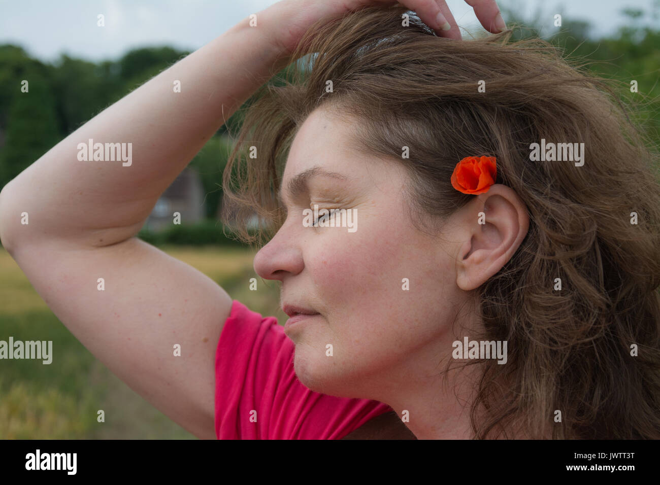 Eine Frau in einer rosa Top ihr Haar nach hinten gezogen, ein wildes Feld Mohn zu offenbaren, versteckt hinter Ihr Ohr an einem Sommertag. Großbritannien Stockfoto