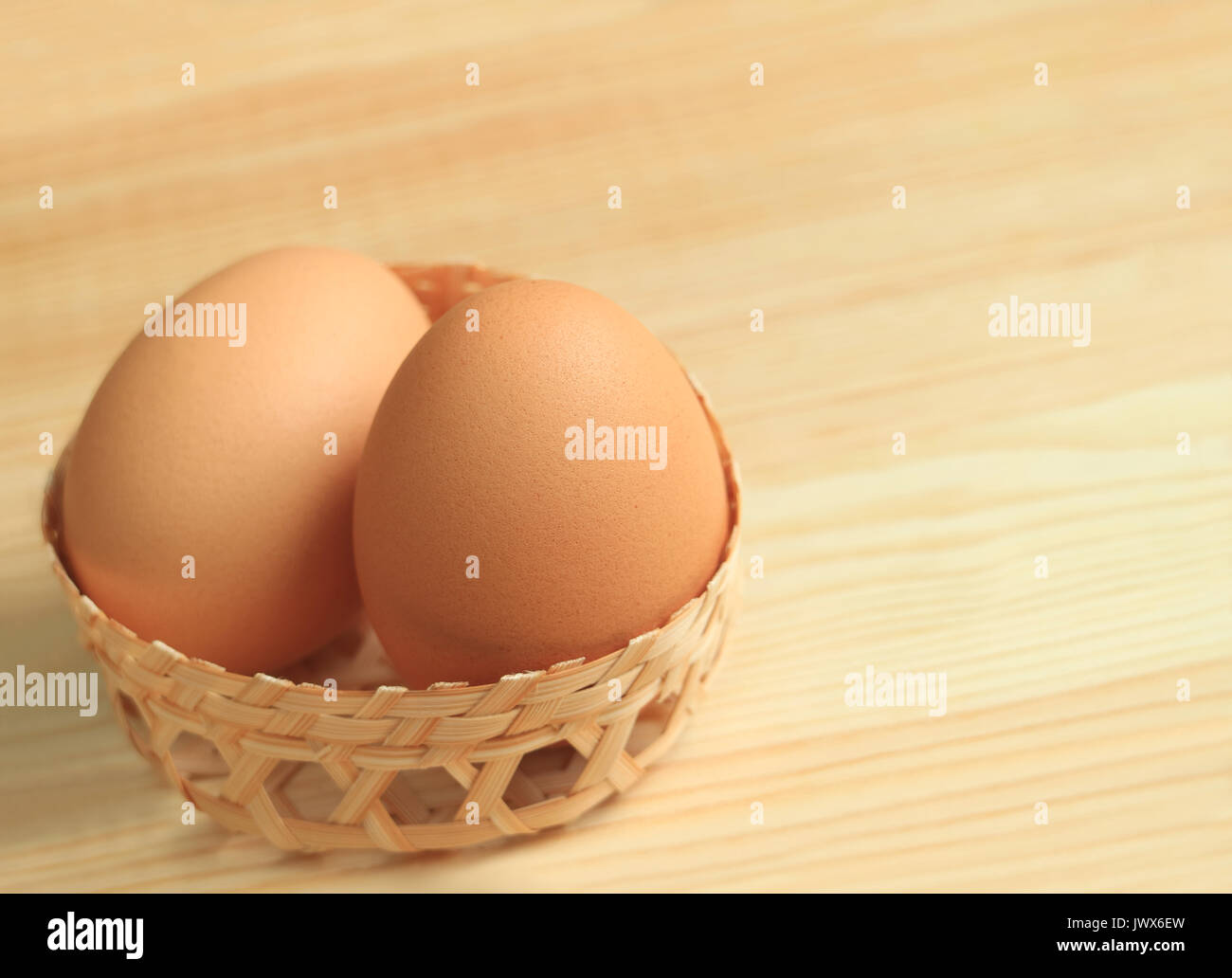 Paar Frische Hühnereier in einem kleinen Weidenkorb auf dem hölzernen Tisch, mit Freiraum für Text und Gestaltung Stockfoto