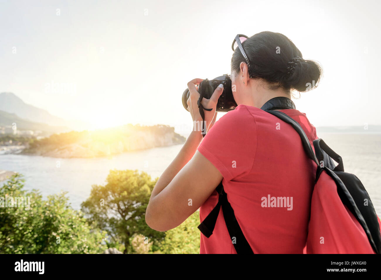 Eine Frau mit Kamera fotografieren den Sonnenuntergang an der Küste. Stockfoto