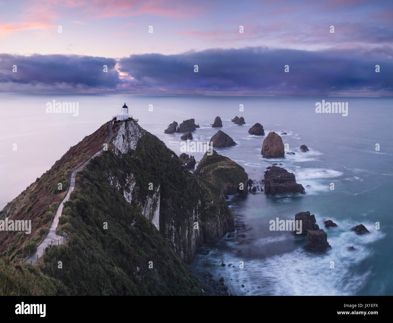 Nugget Point Lighthouse Beratung auf dem Weg zu den fernen Pause in der stürmischen Wolken. Neuseeland. Otago. South Island. Die Catlins. Stockfoto