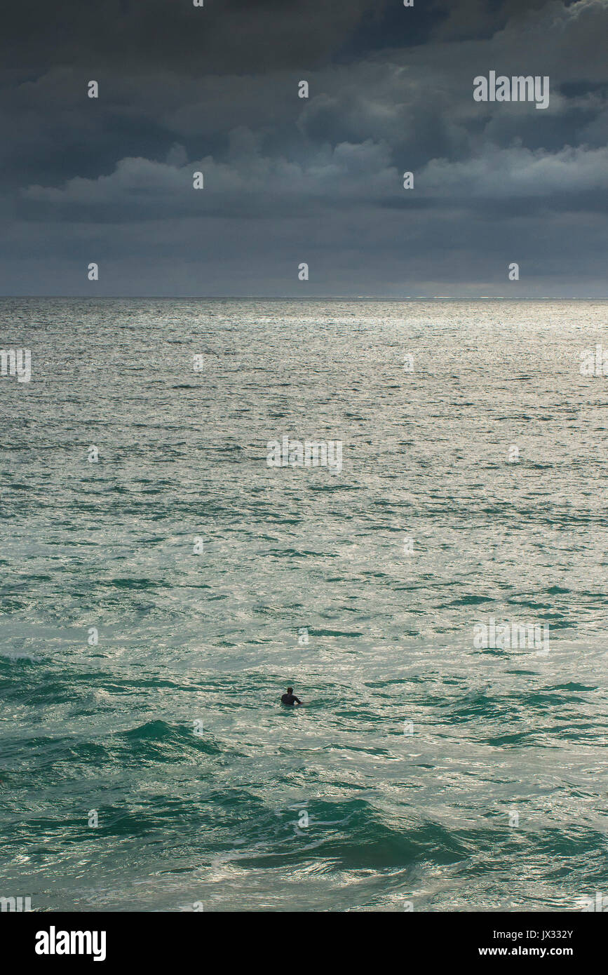 Ein einsamer Surfer wartet auf eine Welle in der weiten, offenen Ozean. Stockfoto