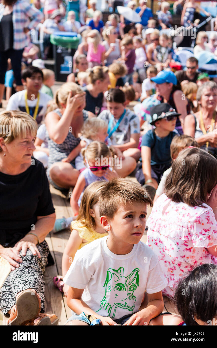 Kinder, meist Grundschulalter, 6-10 Jahre alt, einige Erwachsene, sitzen auf den Terrassen in der Sonne während der Hobby Horse Club Treffen in Broadstairs Folk Woche. Stockfoto
