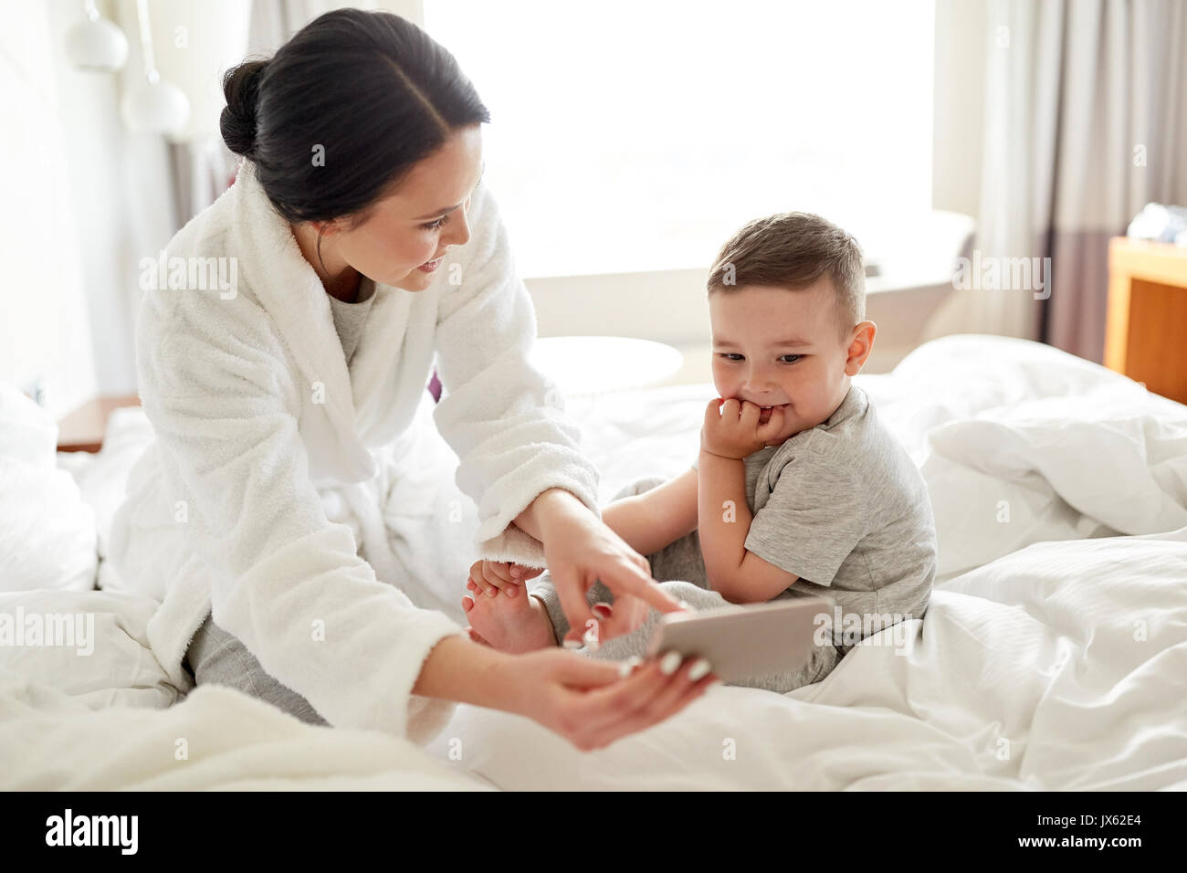Mutter und Sohn mit Smartphone im Bett im hotel Stockfoto