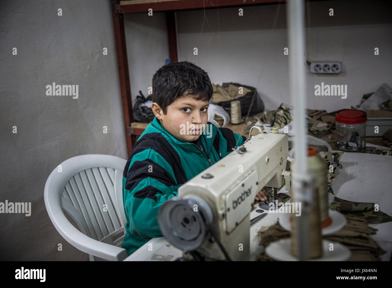 Eine syrische Flüchtlinge Junge in Fabriken in der Türkei arbeiten, jetzt nach Hause zu über 2,7 Millionen Syrer. Die kleine Textil shop, wo er und andere Jungen, Mädchen und Männer beschäftigt sind produziert Uniformen und Rucksäcke, die an den verschiedenen kriegführenden Parteien in Syrien verkauft werden. Die Armut treibt viele Familien ihre Kinder zur Arbeit anstatt zur Schule. Bildungschancen für die Syrer in der Türkei sind auch begrenzt. Stockfoto