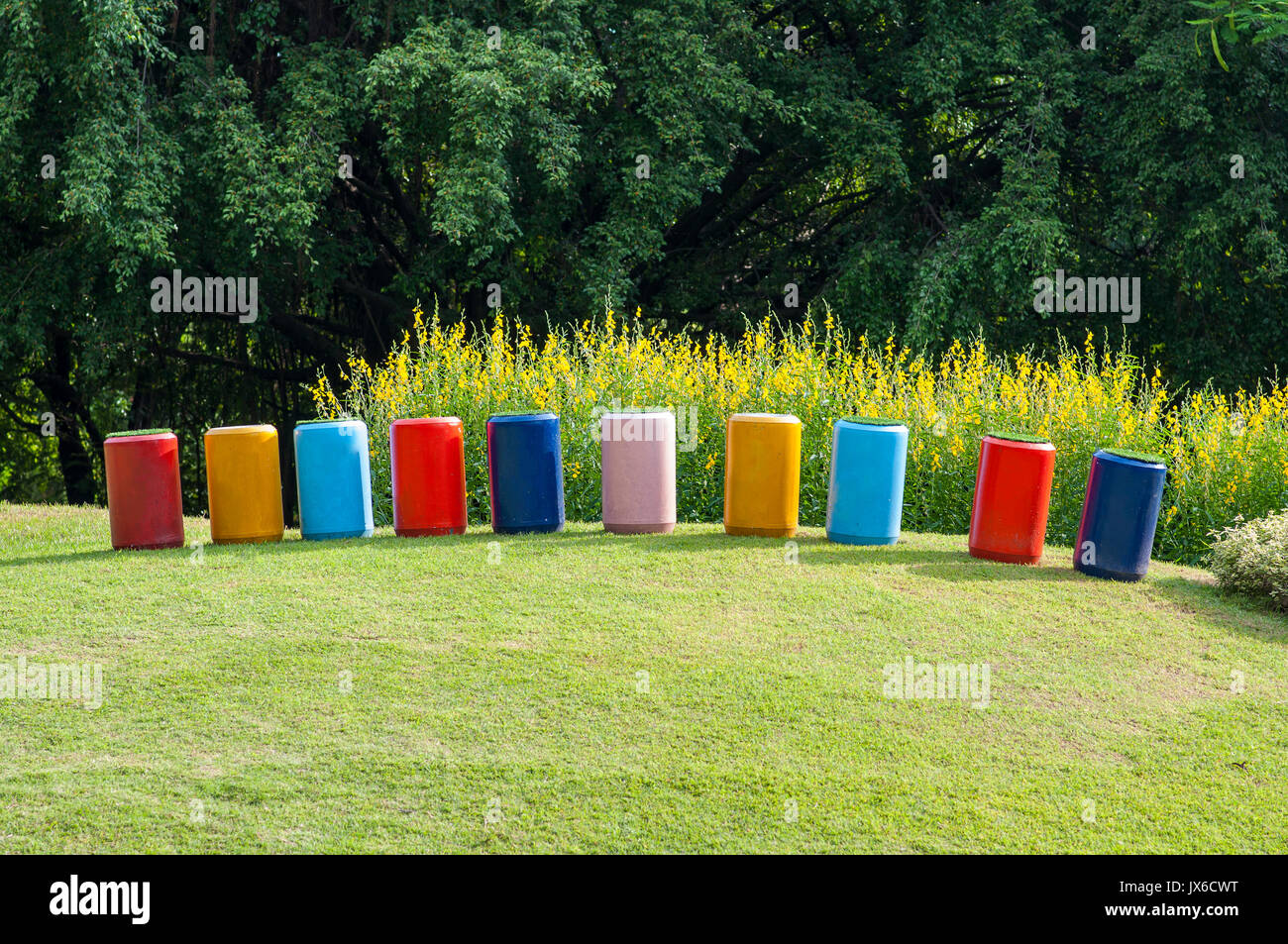 Dekorieren Multi Color konkrete Leitung stehen auf Gras im Park. Gruppe von gelben Blumen, die Bush am Damm Hang grünes Gras. Stockfoto