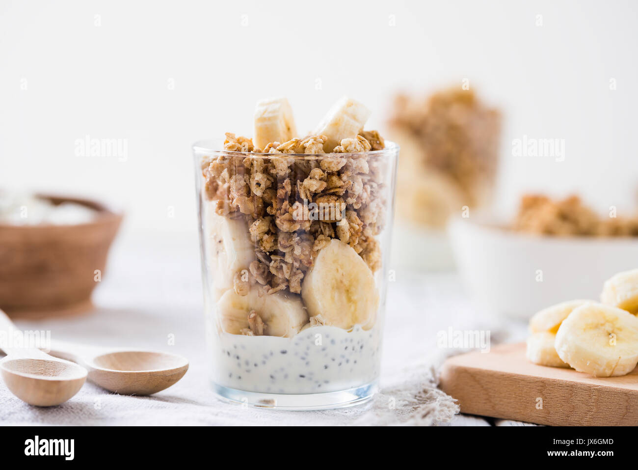 Chia pudding Parfait, mehrschichtige Joghurt mit Banane, Müsli. Gesundes Frühstück Konzept auf weissem Holztisch Stockfoto