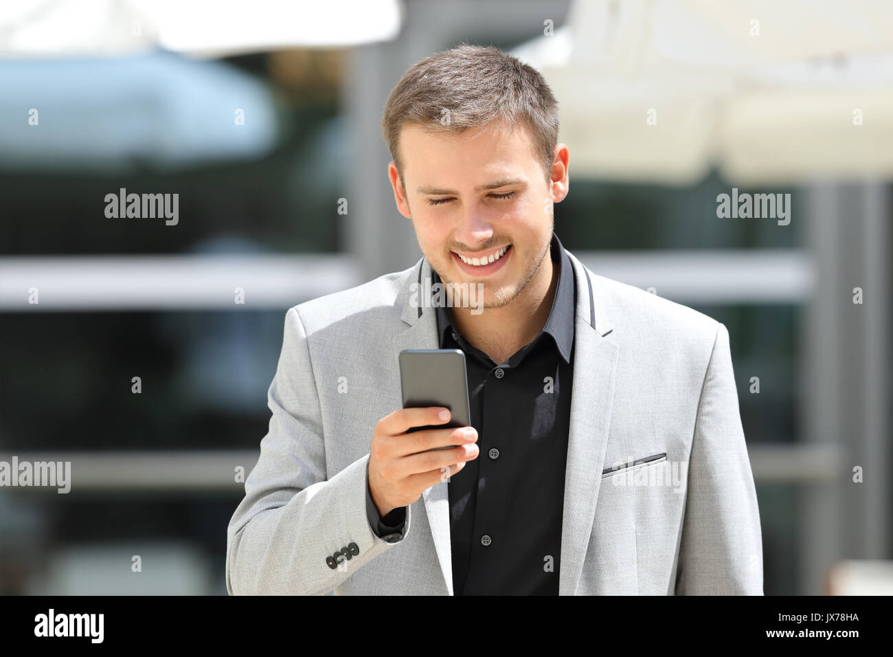 Vorderansicht Porträt einer jungen Geschäftsmann zu Fuß in Richtung Kamera und SMS auf dem Telefon Stockfoto