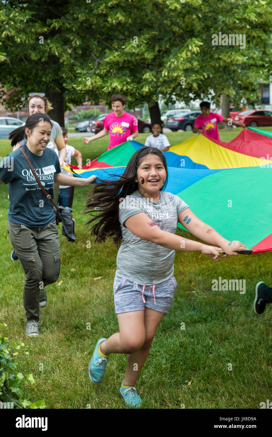 Detroit, Michigan - Kinder und junge erwachsene Freiwillige spielen mit einem großen Fallschirm Tuch in der Clark Park. Stockfoto