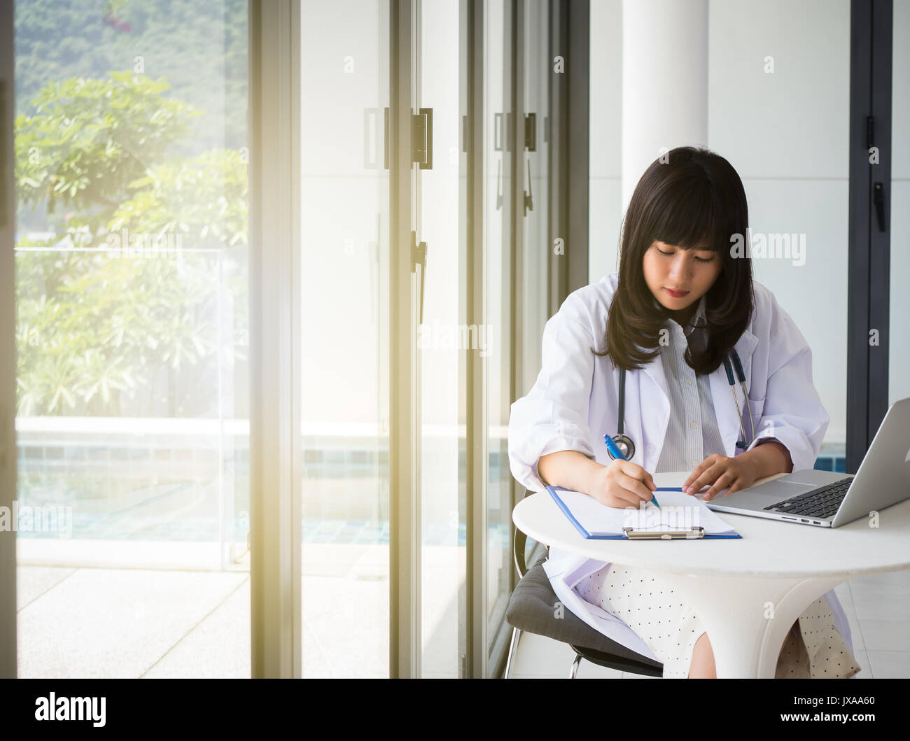 Junge Asien Arzt schreibt einen Bericht für einen Bestrahlungsplan mit Stethoskop, die Hand am Stift und Informationen mit Laptops im Gesundheitswesen finden Stockfoto