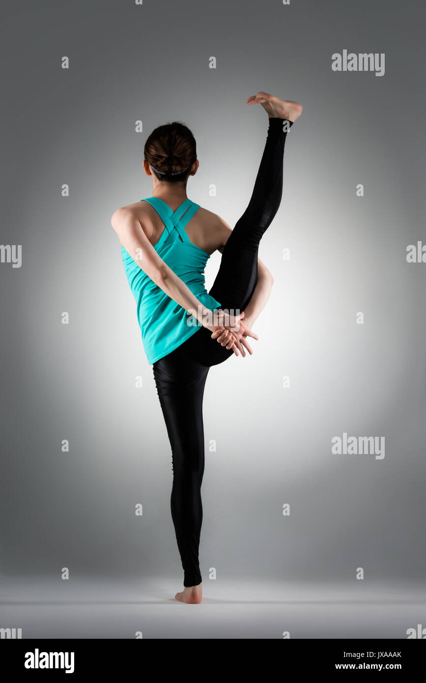 Rückansicht Foto von jungen weiblichen Yoga mit einem Bein in der grauen Hintergrund und Stretching Körper mit Händen player. Stockfoto