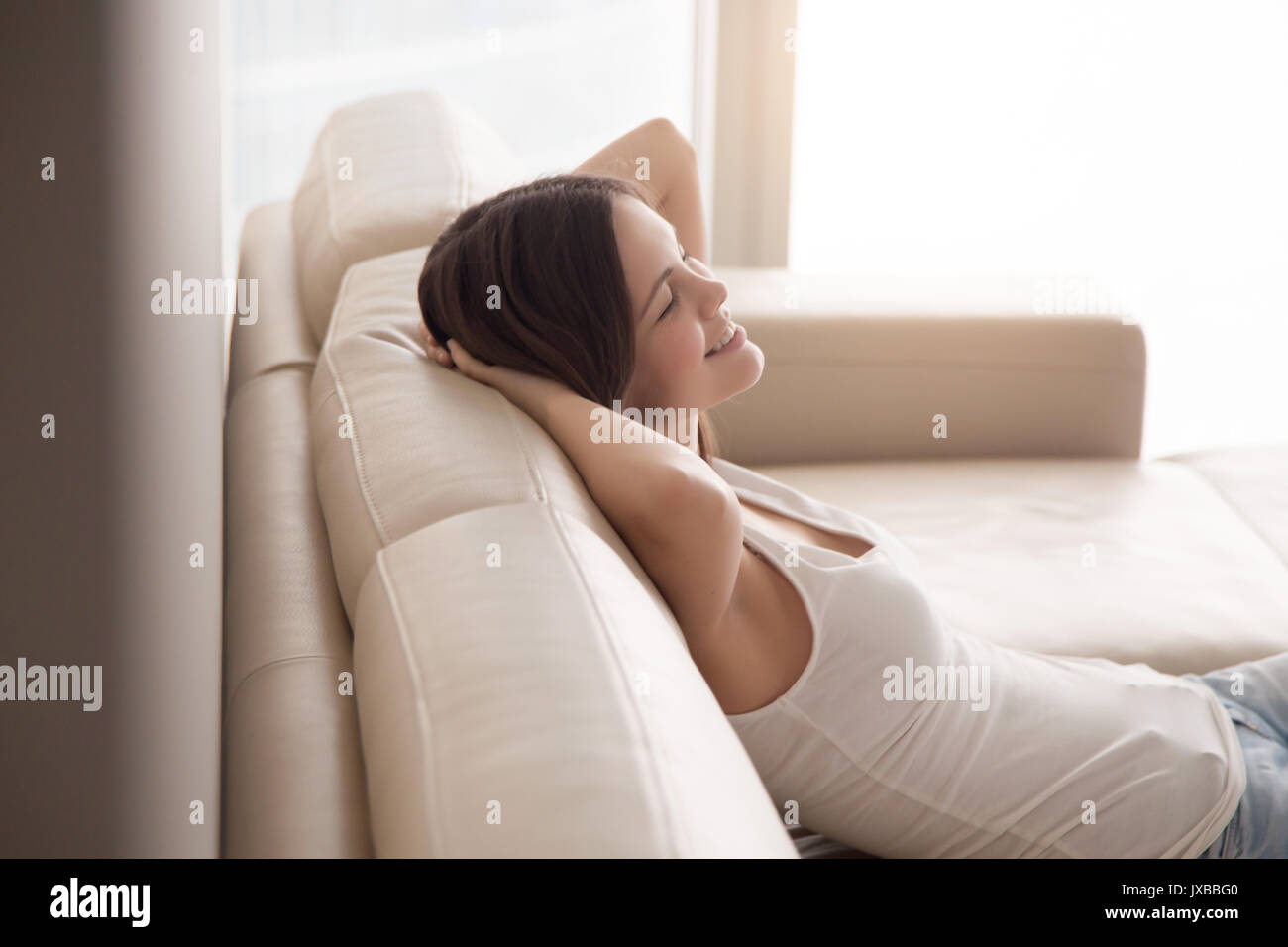 Glückliche junge Frau sitzt auf der bequemen Couch, Hände hinter Hea Stockfoto