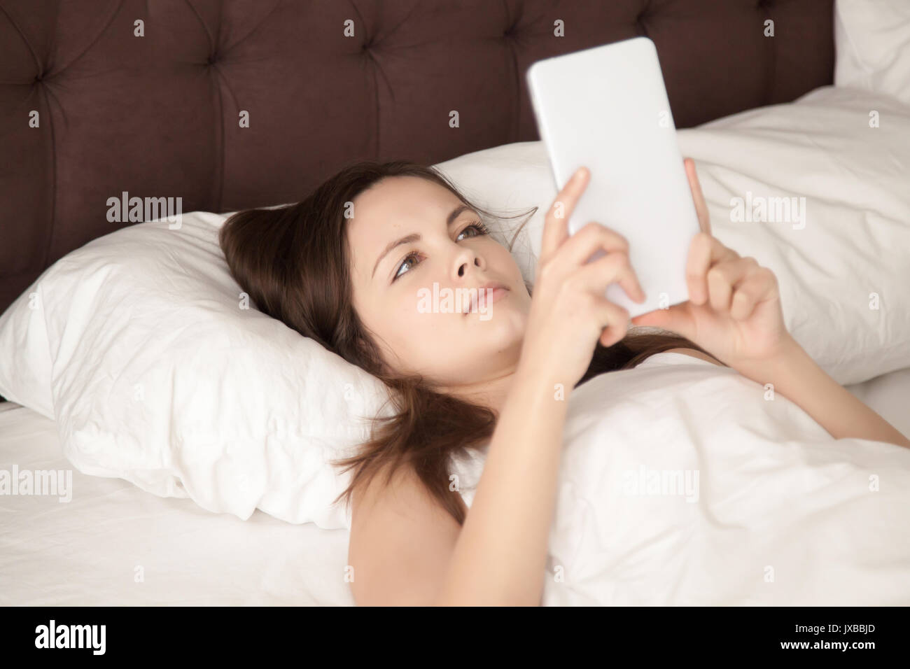 Junge Frau mit digitalen Tablet im Bett liegt, das Lesen von E-Books Stockfoto
