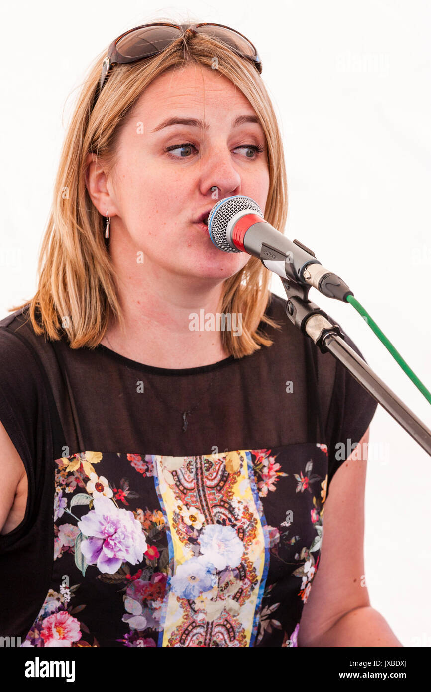 Junge kaukasier blonde Frau, 20s, sitzen im Freien, in das Mikrofon singen, Sonnenbrille auf dem Kopf. Mitglied des Samba Azul music group. Stockfoto