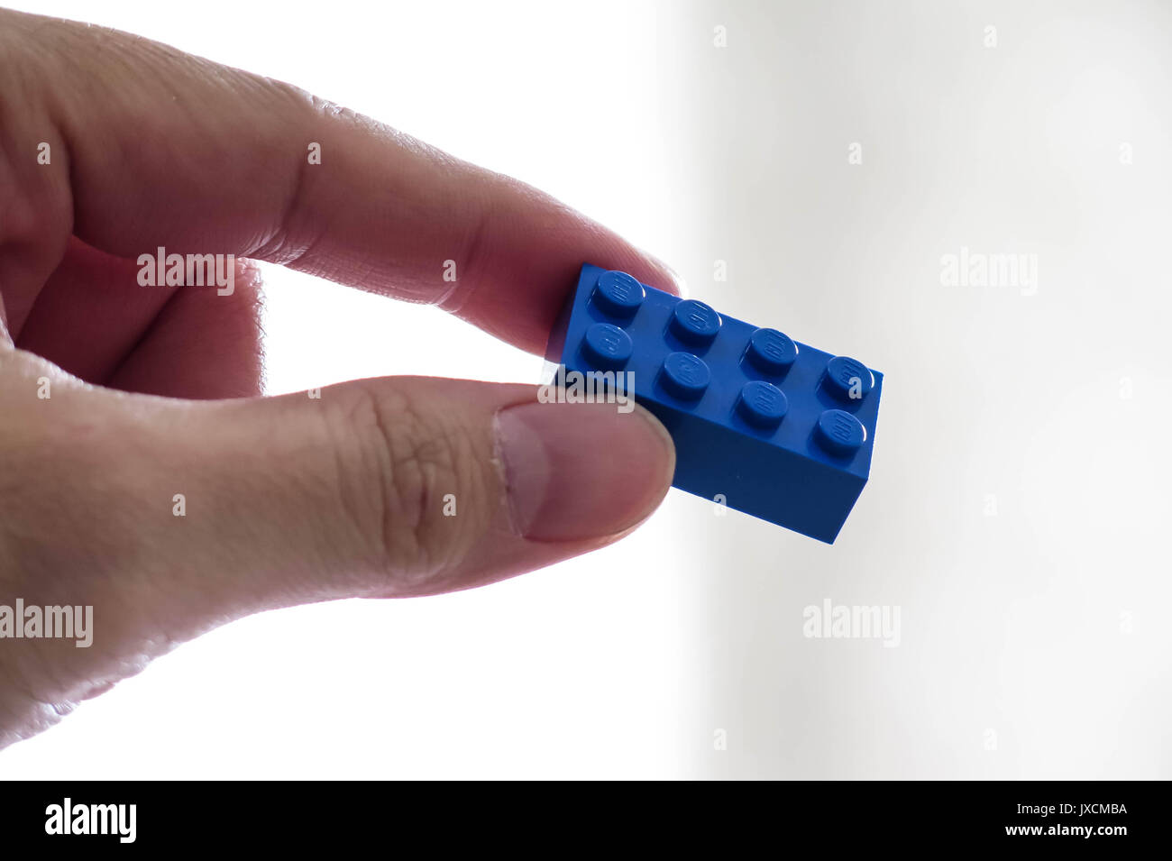 Hand mit einem einzigen blauen Lego Spielzeug Ziegel auf einen hellen Hintergrund. Stockfoto