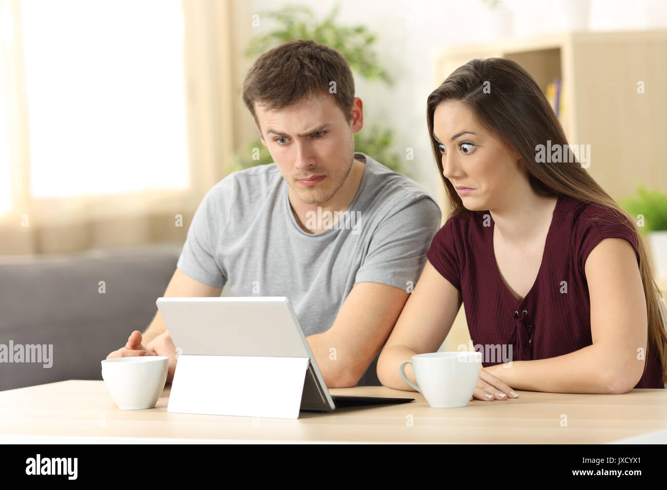 Verwirrt Paar empfangen auf Nachrichten in einem Schreibtisch zu Hause sitzen Stockfoto