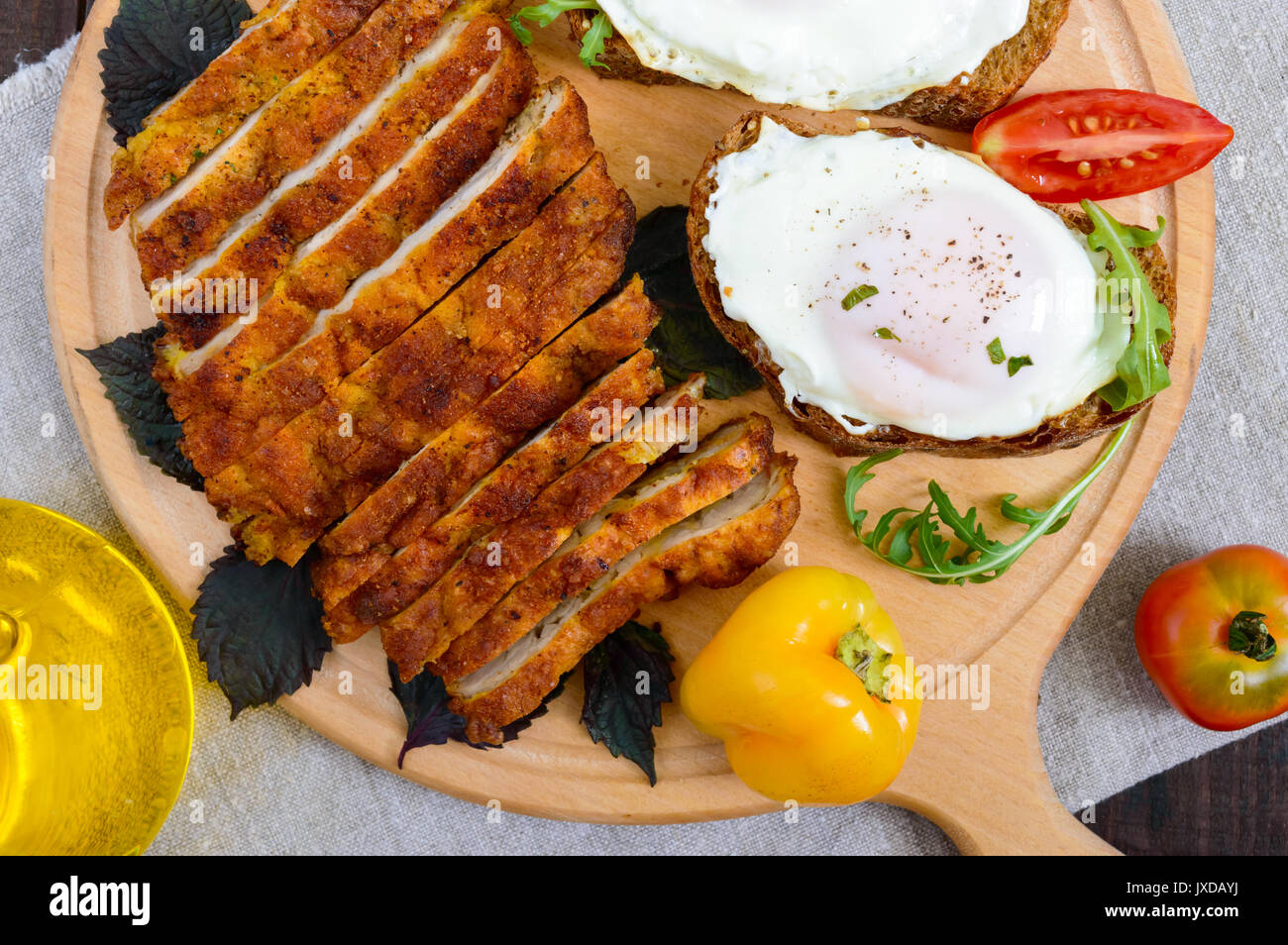 Stücke von Chop (Schnitzel), Toast mit Eiern, frischen Tomaten auf einem Holzbrett auf einem dunklen Hintergrund. Ansicht von oben. Stockfoto