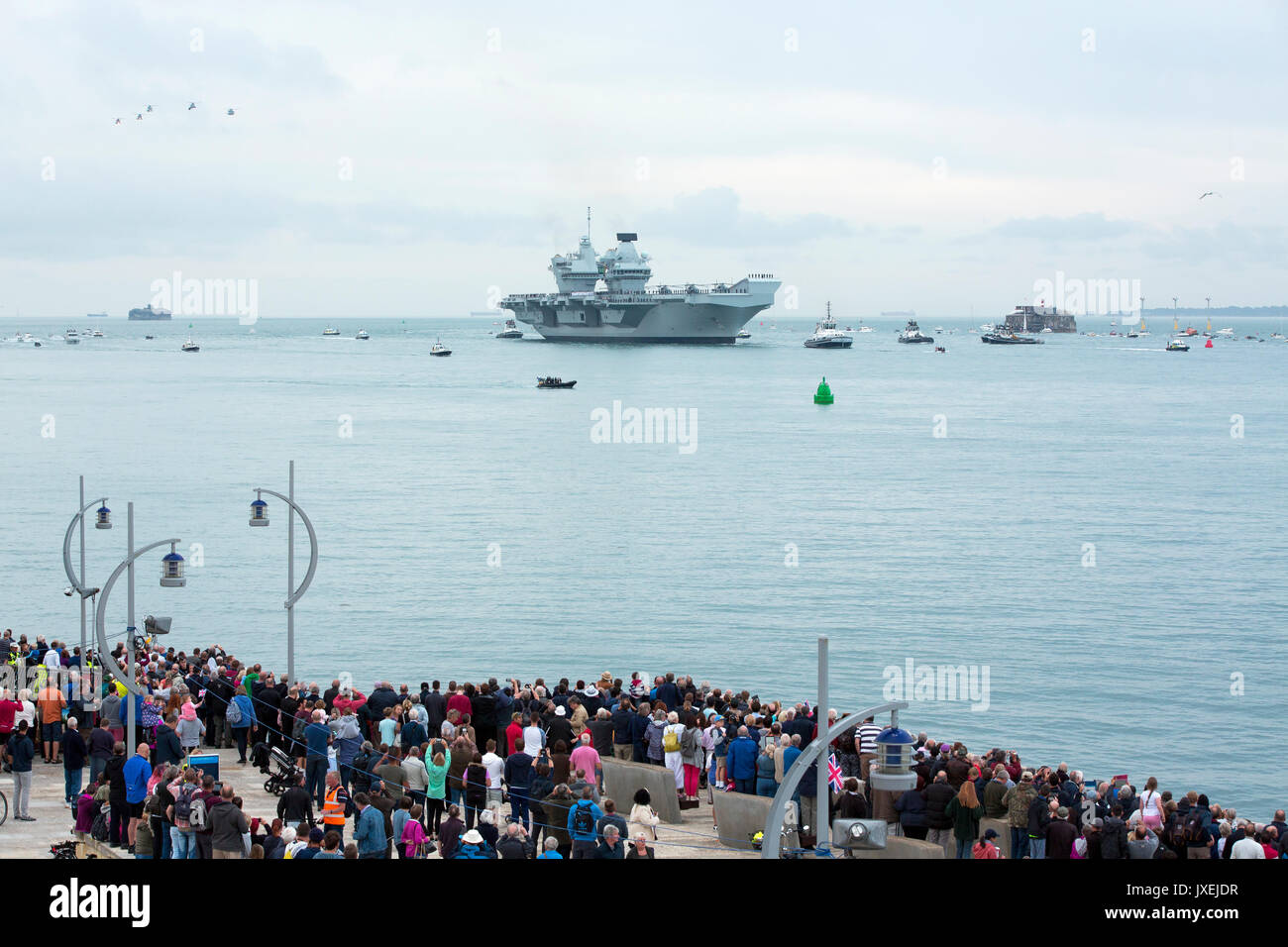 Portsmouth, Großbritannien. 16 Aug, 2017. HMS Queen Elizabeth segeln in Portsmouth Es ist Heimathafen für die erste Zeit. Große Menschenmenge auf dem Meer Wand einladende neueste und größte Kriegsschiff in Großbritannien. Flug der Hubschrauber von der Begleitung des Flugzeugträger Overhead. Quelle: David Robinson/Alamy leben Nachrichten Stockfoto