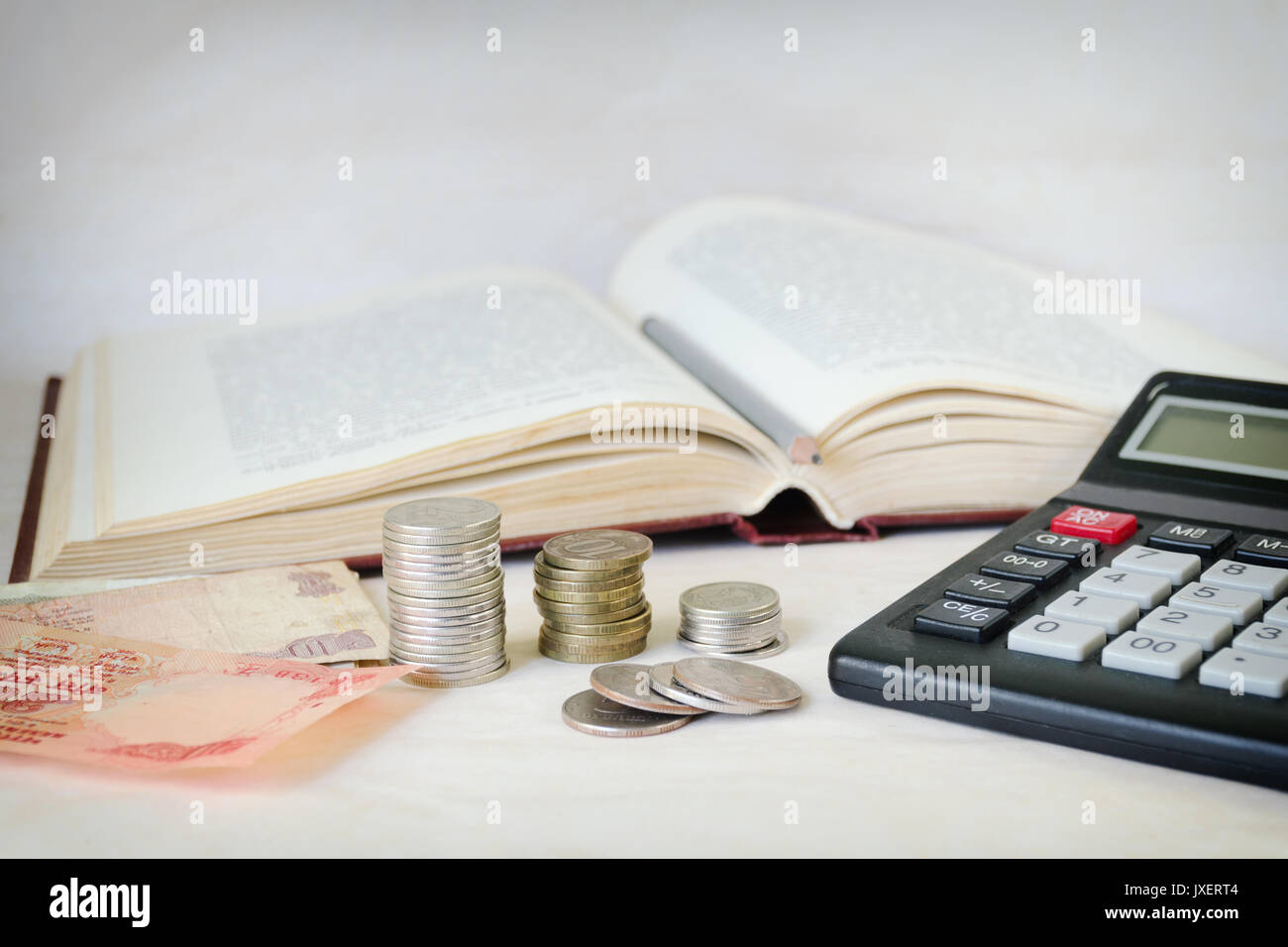 Geldscheine, Stapel von Münzen und einen Rechner vor ein offenes Buch. Das Konzept der teure Bildung und Gelehrsamkeit Stockfoto