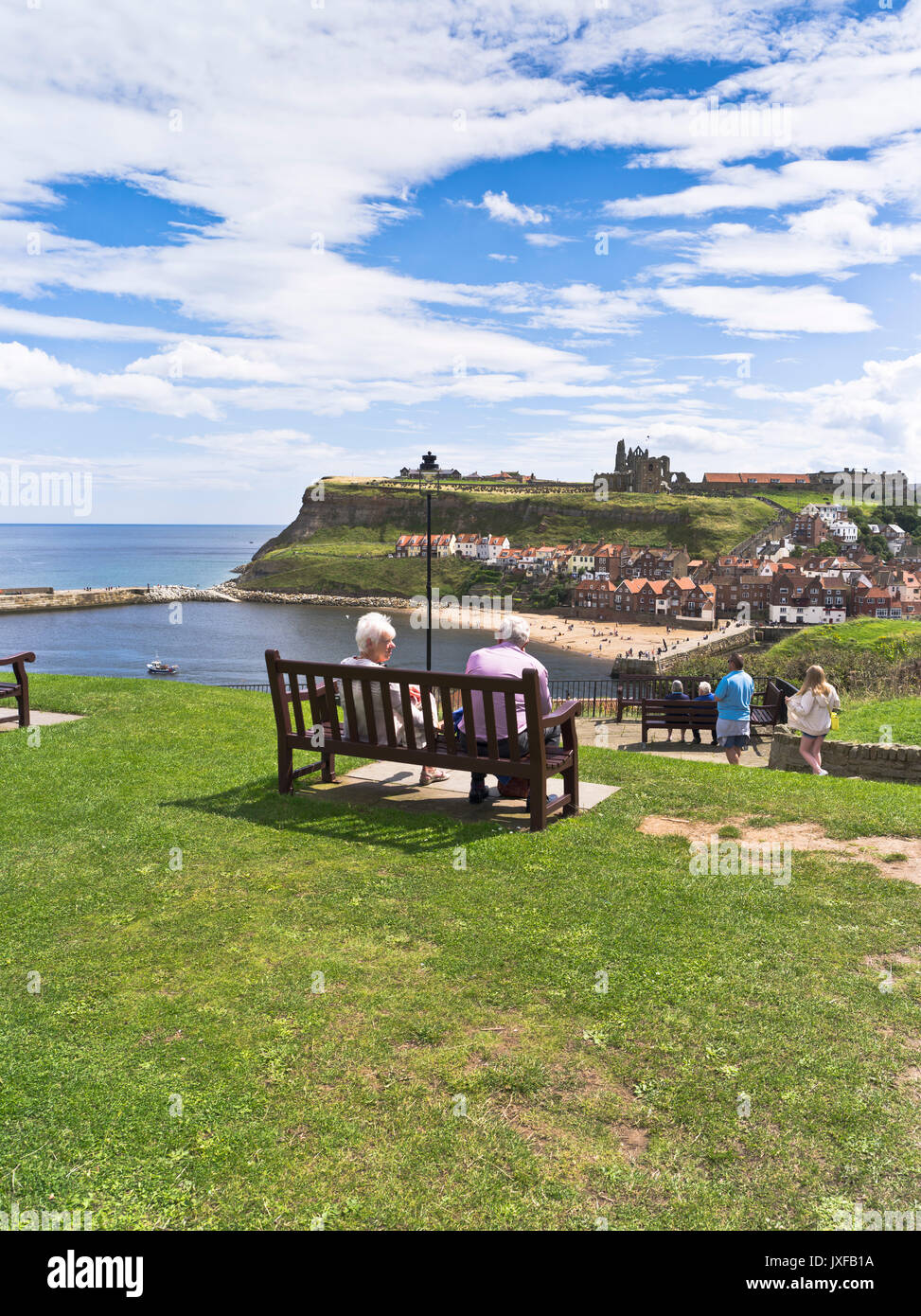 dh Britain Stadthafen WHITBY NORTH YORKSHIRE Menschen sehen Paar Sitzen mit Blick auf Abtei Sommer englisch Tourismus Urlaubsbank aus Westen Klippe Stockfoto